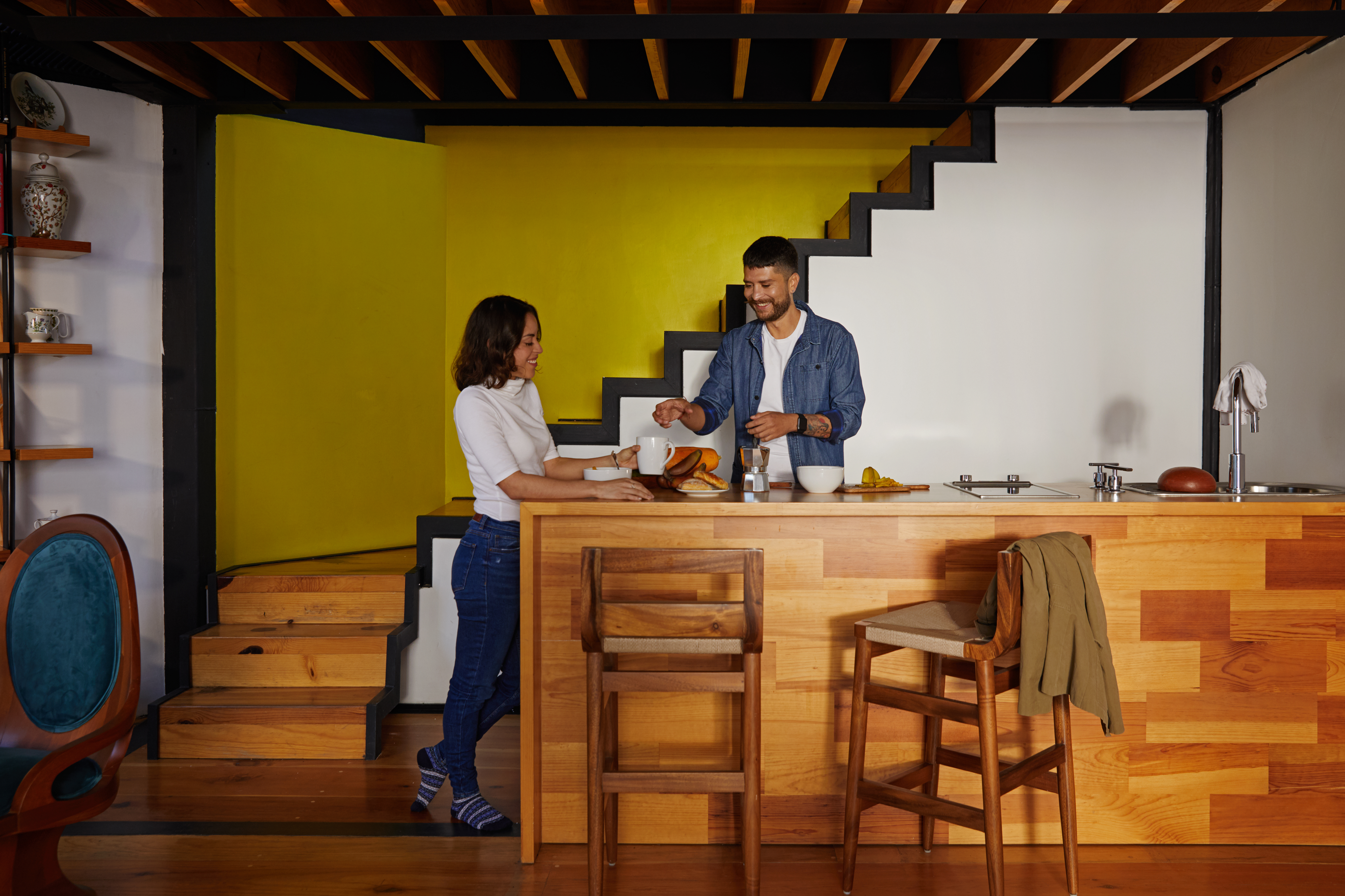 Two people enjoying coffee at a modern kitchen island with a wooden design and yellow accent wall.