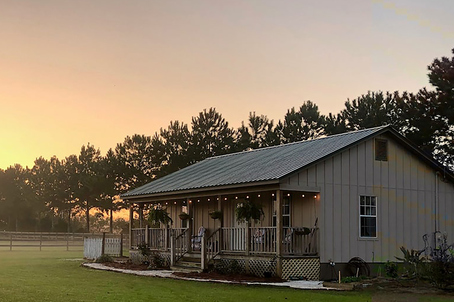 Sun setting over a ranch home surrounded by trees.