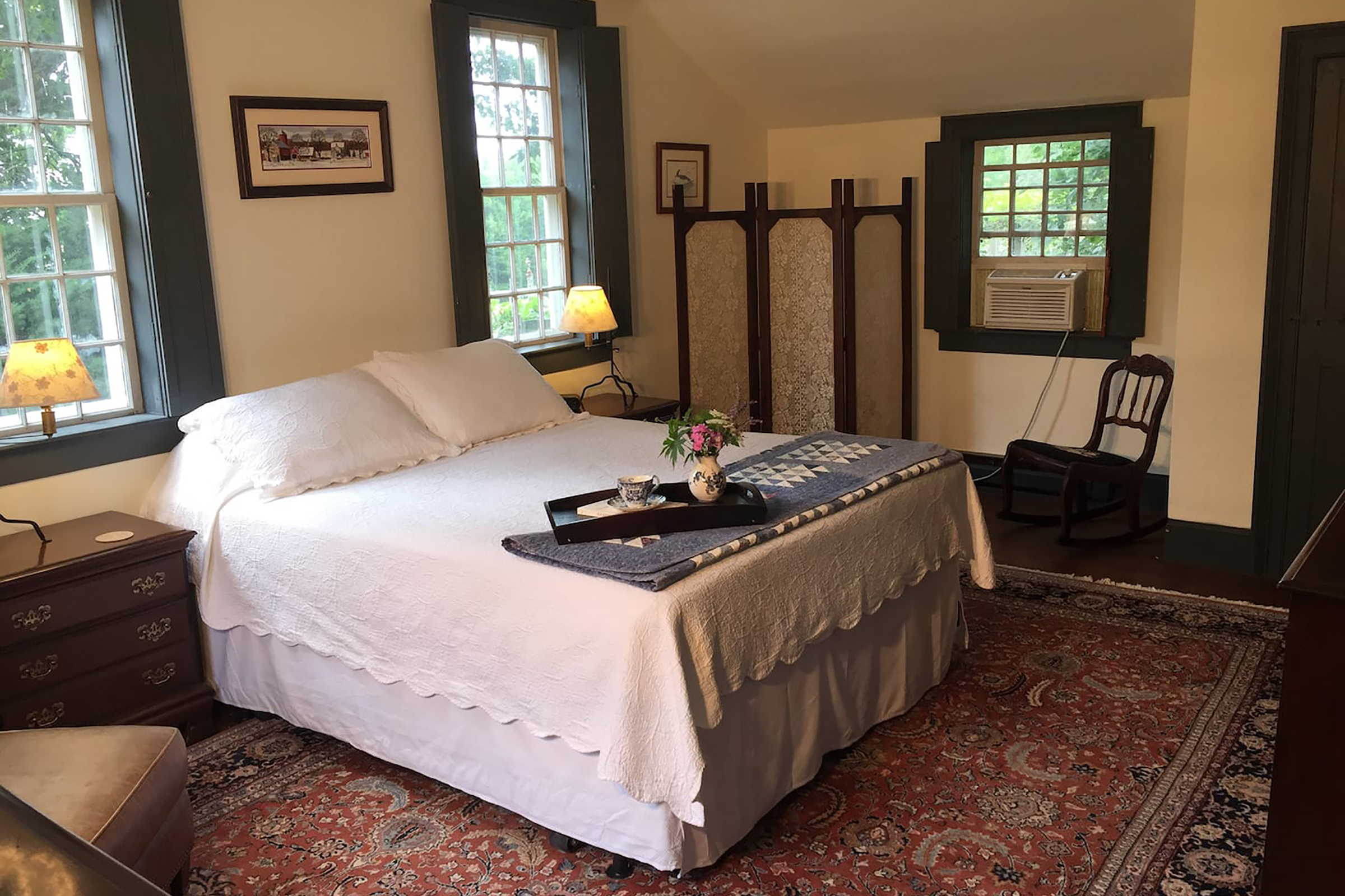 A queen bed with a blue, folded blanket and serving tray set atop the end of the bed. 