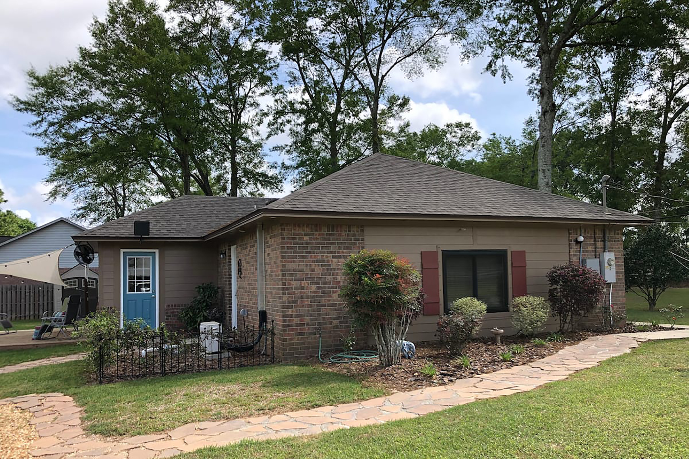 A brown tan and brick ranch style home with red shutters and a blue front door.