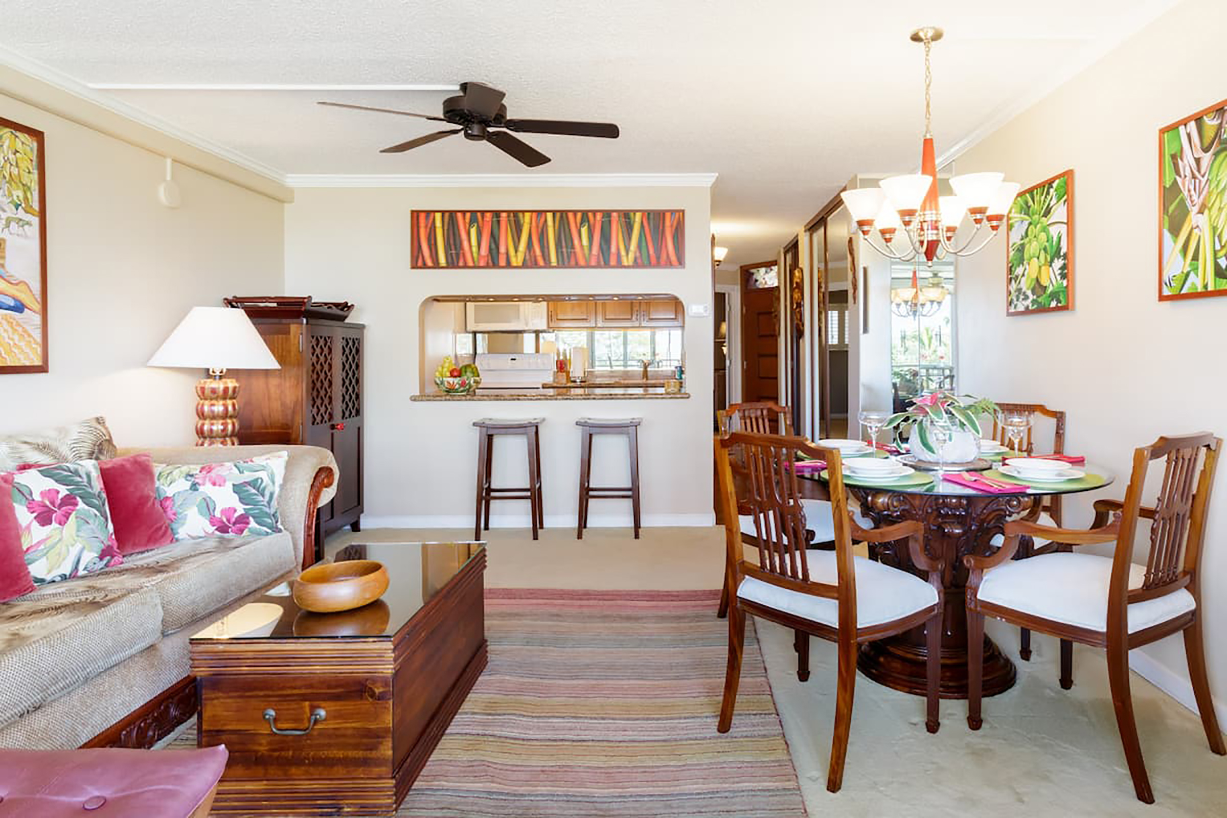 A living room with tropical artwork along the walls, a tan couch and 4-seat dining table. 
