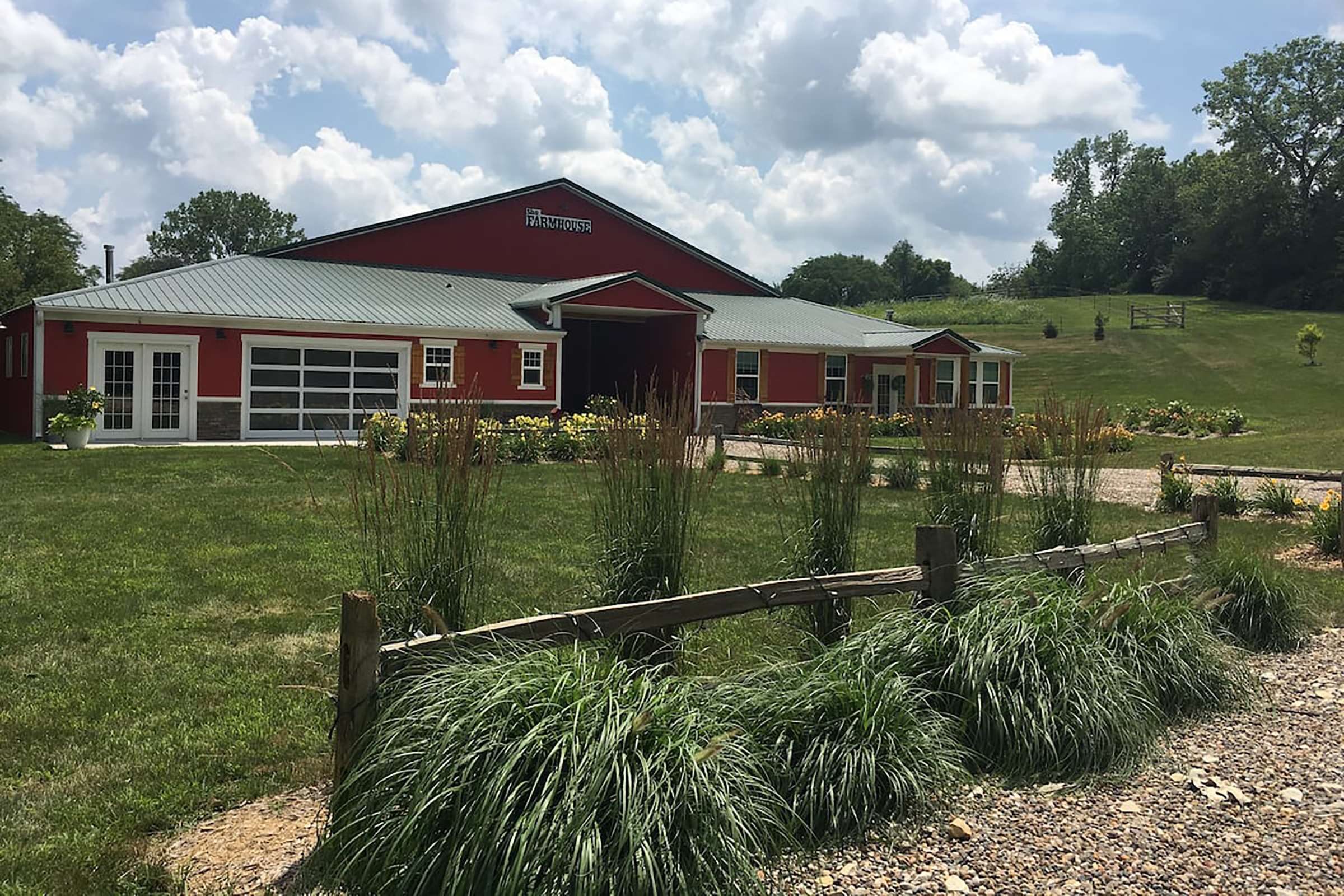 A red farmhouse on an expansive plot of land with yellow flowers lining the house.
