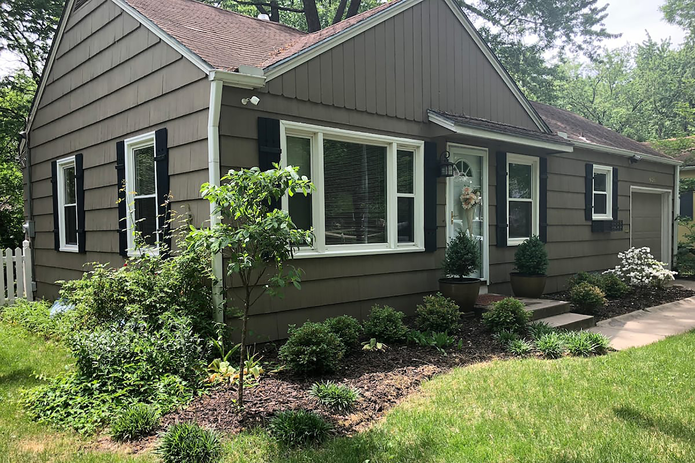 A brown ranch home with black shutters and a white front door.