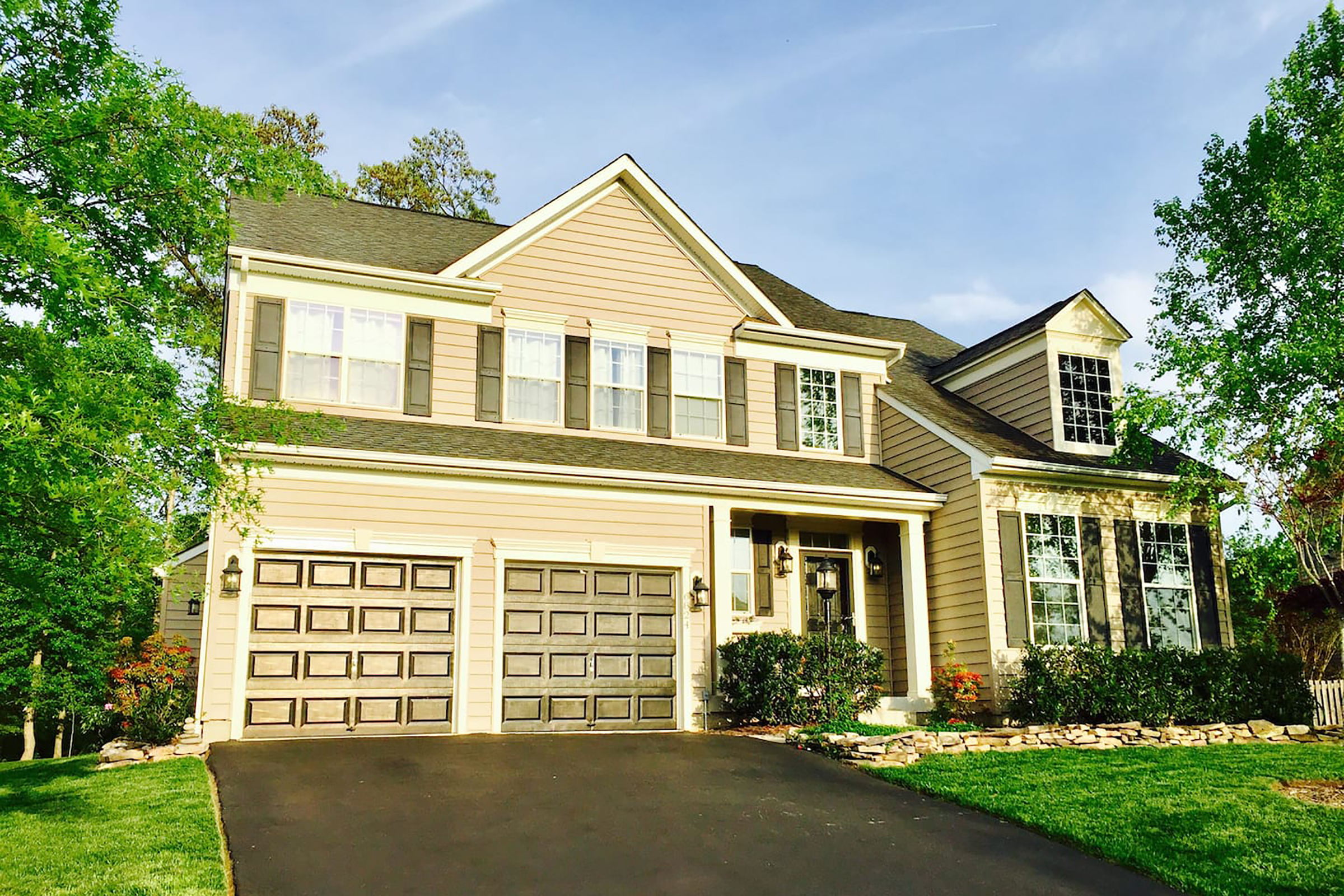 A tan colored contemporary two story home with a two car garage and a black driveway. 