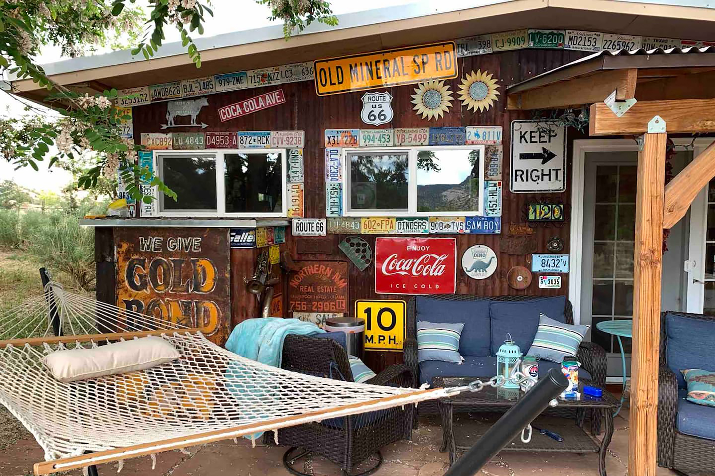 A hammock sits in front of the home that is lined with historical signs, including coca-cola advertisements and vintage license plates