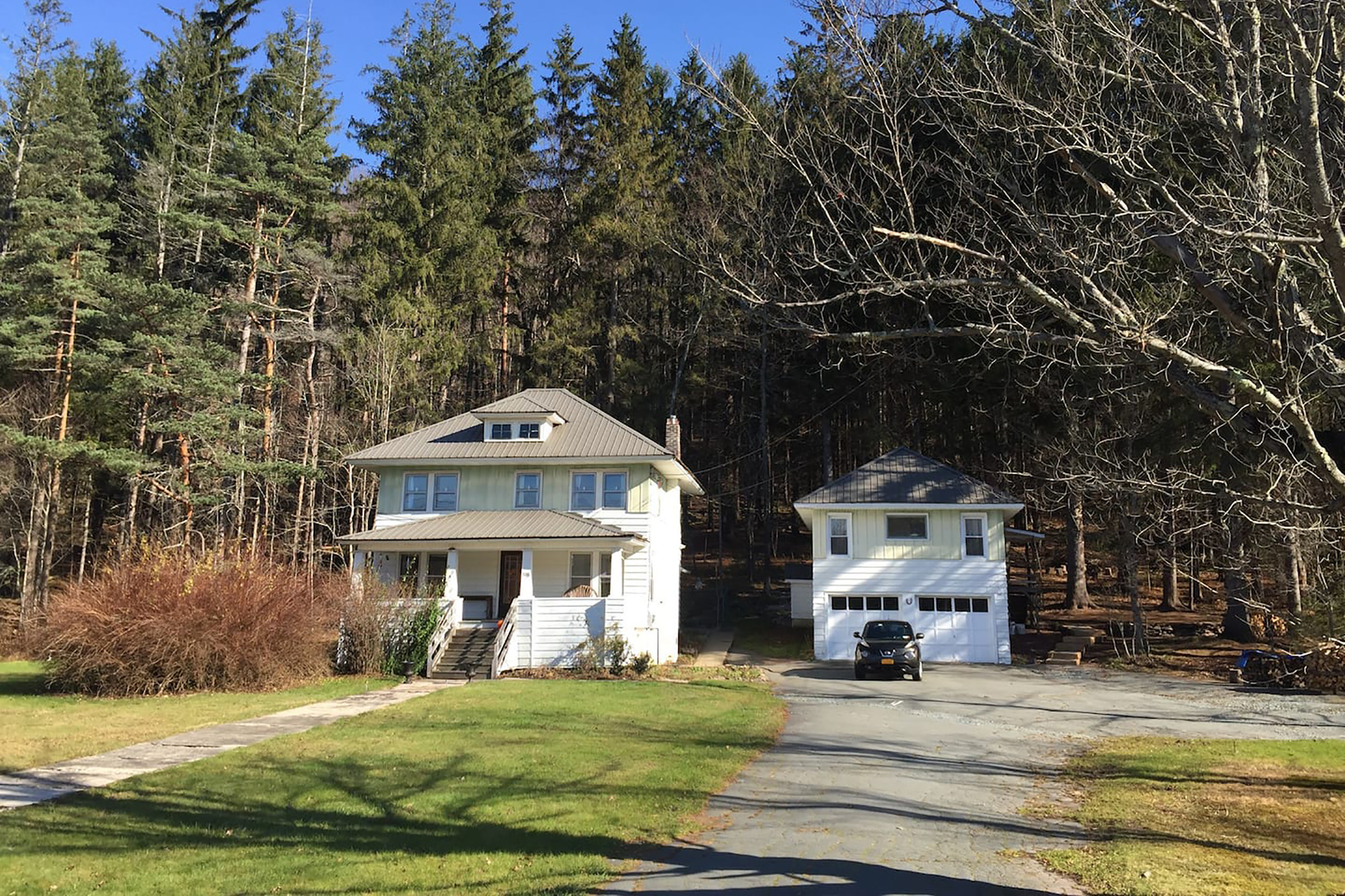 A two story home with a front porch next to a guest home with an attached garage and car parked out front. 