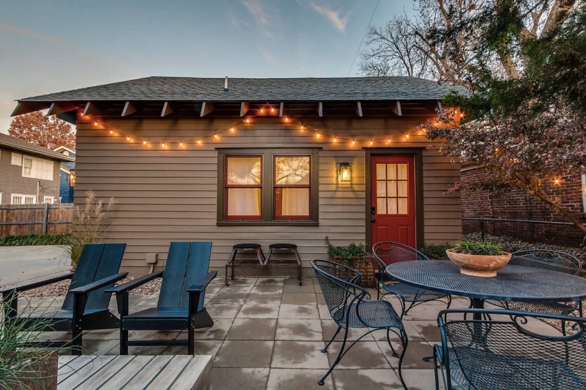 A tan colored home with a red door and illuminated string lights hanging in front