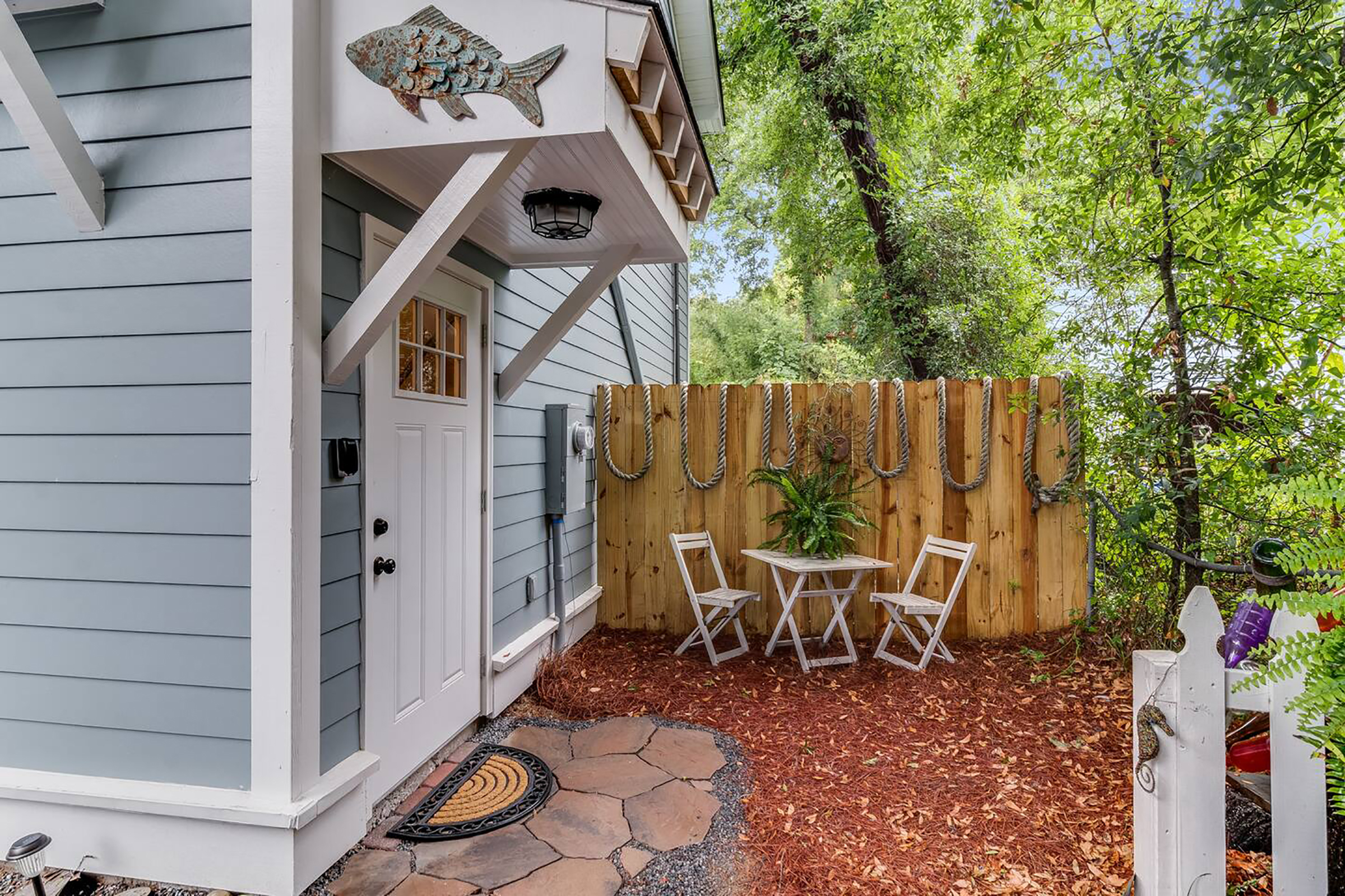 The entrance to a light blue home with artwork of a fish hanging on the side.
