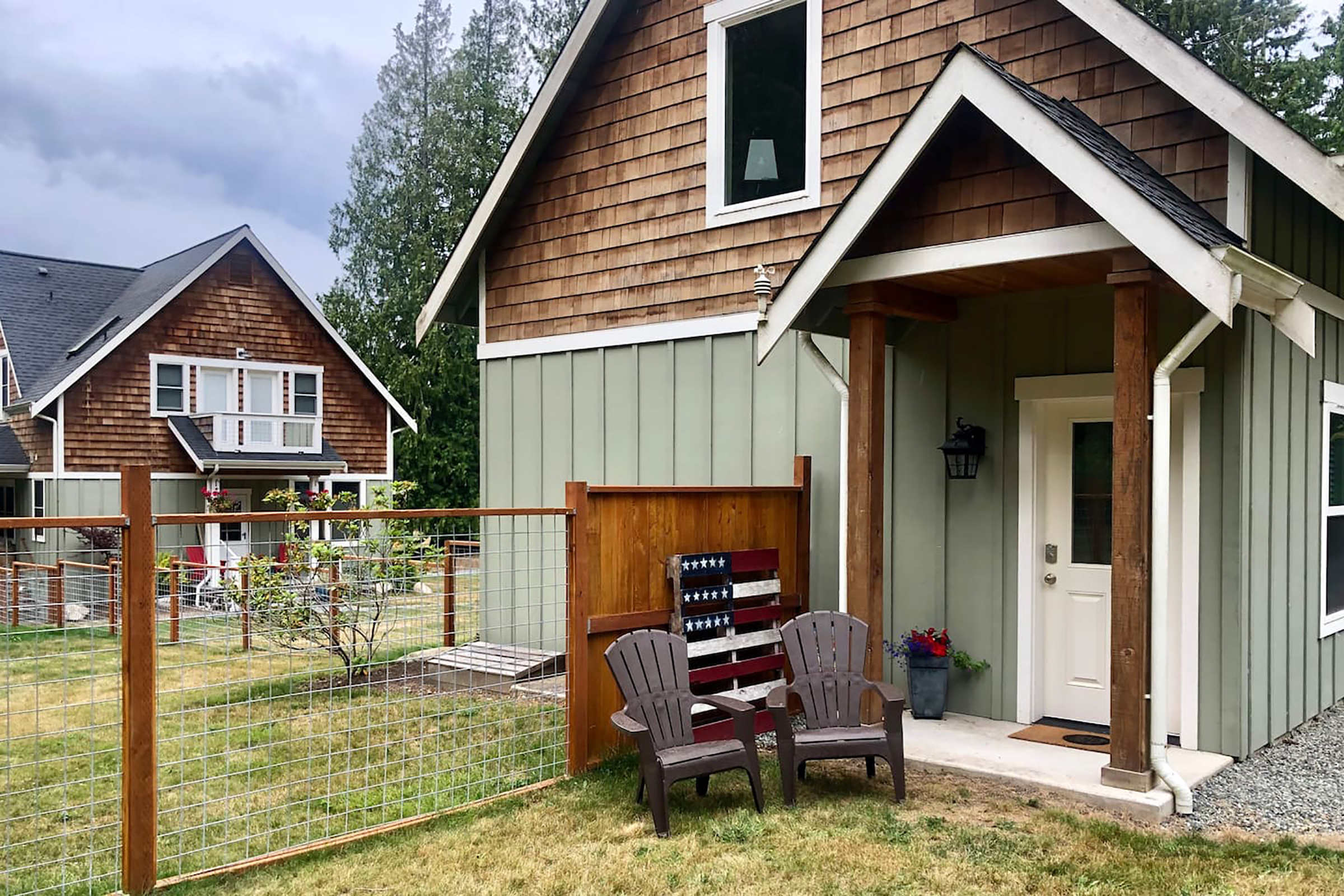 A home with brown shingles and green siding with two lounge chairs out front.