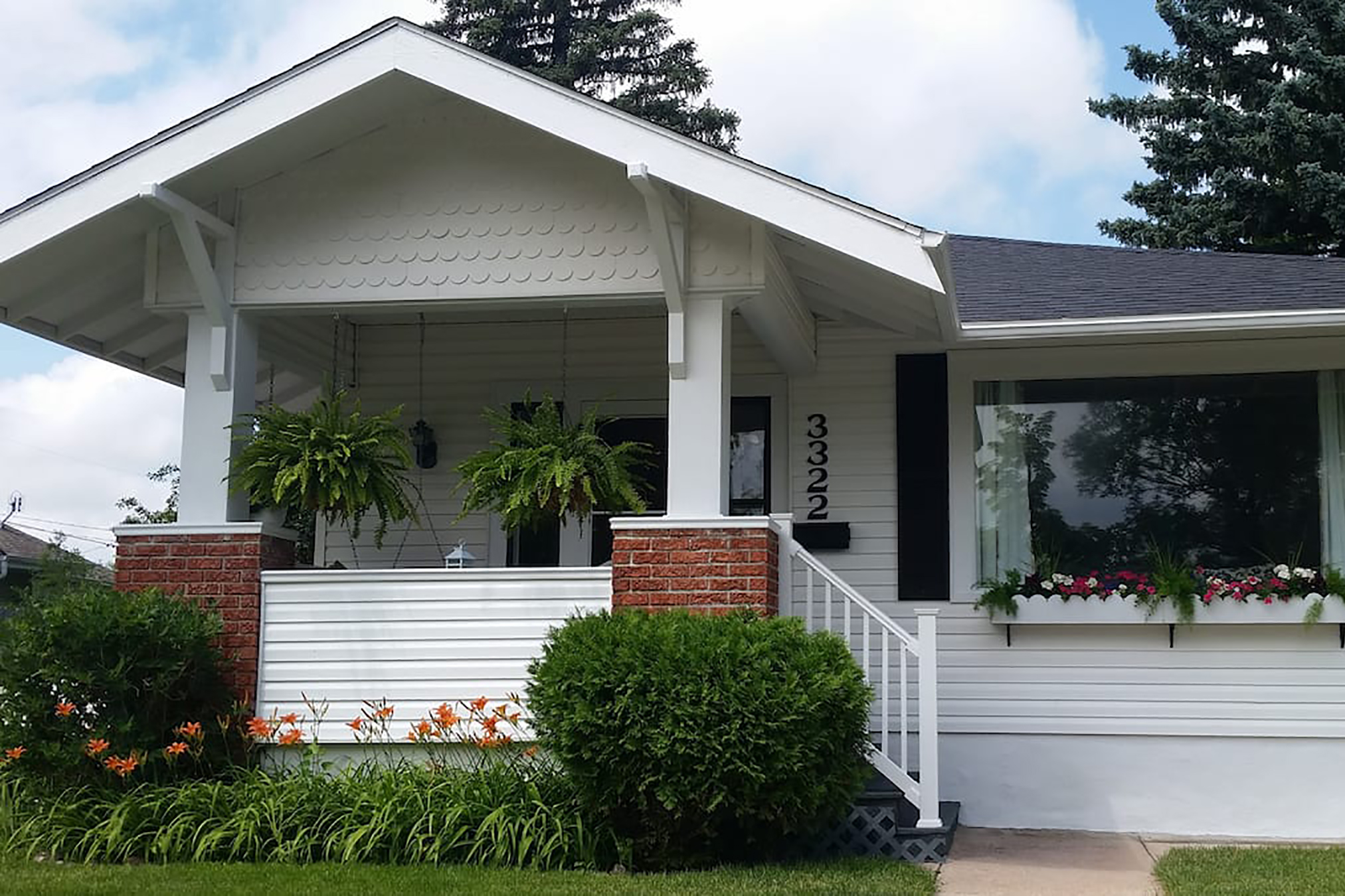 A white home with stairs leading to the entrance and a bed of flowers at the entrance. 
