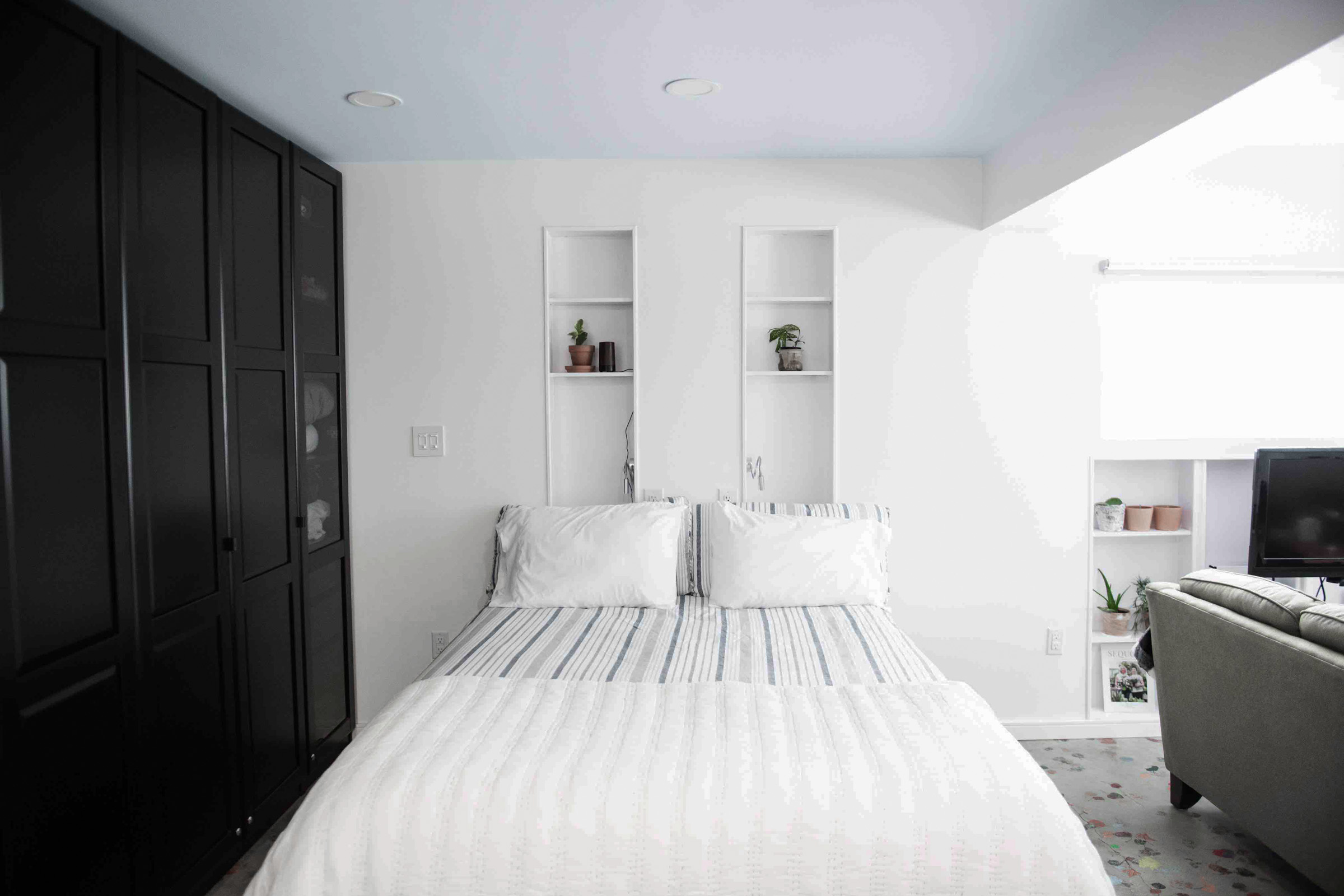 White bed with comforter and striped linens and potted indoor plants