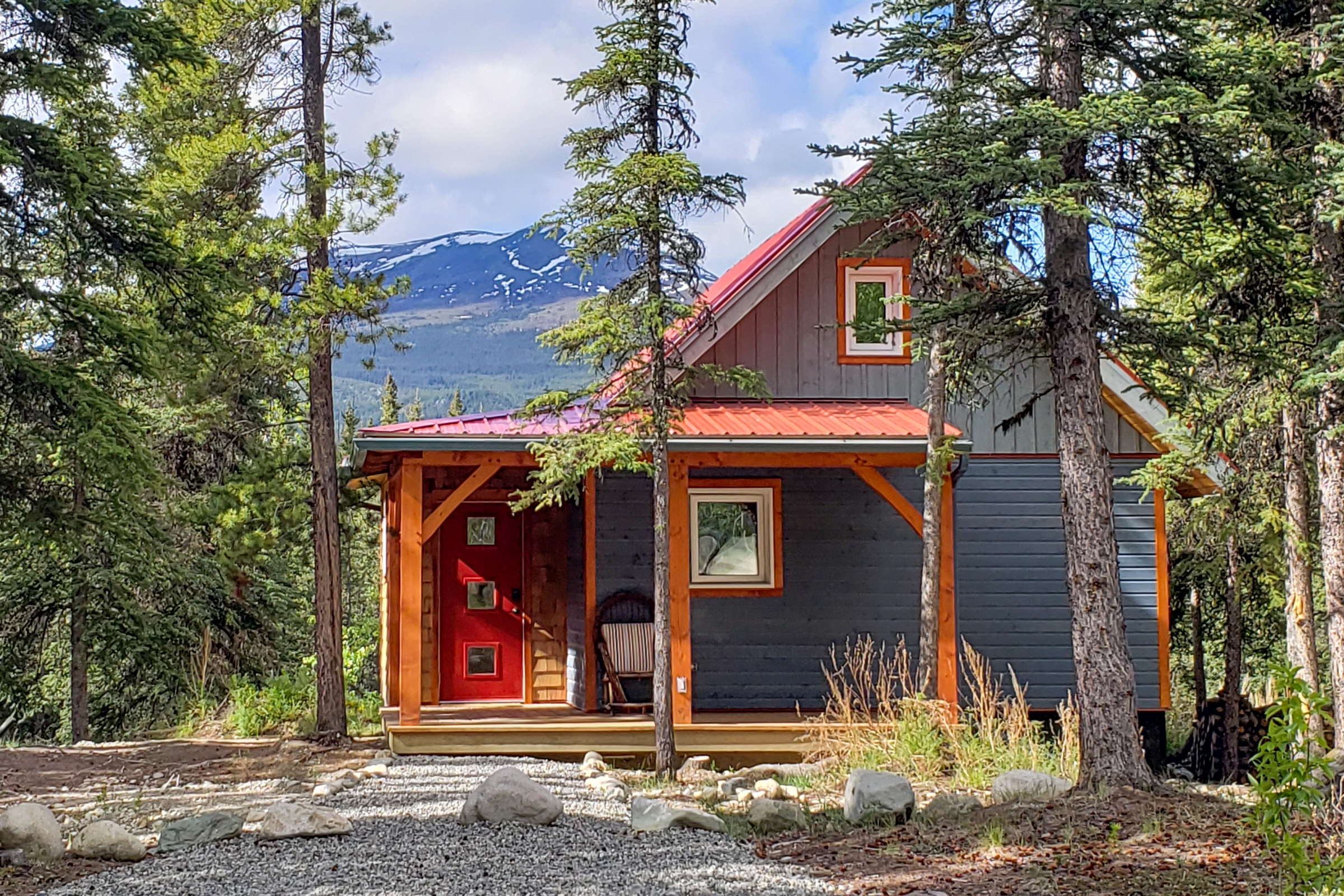 House with red door set in front of a mountainous backdrop 