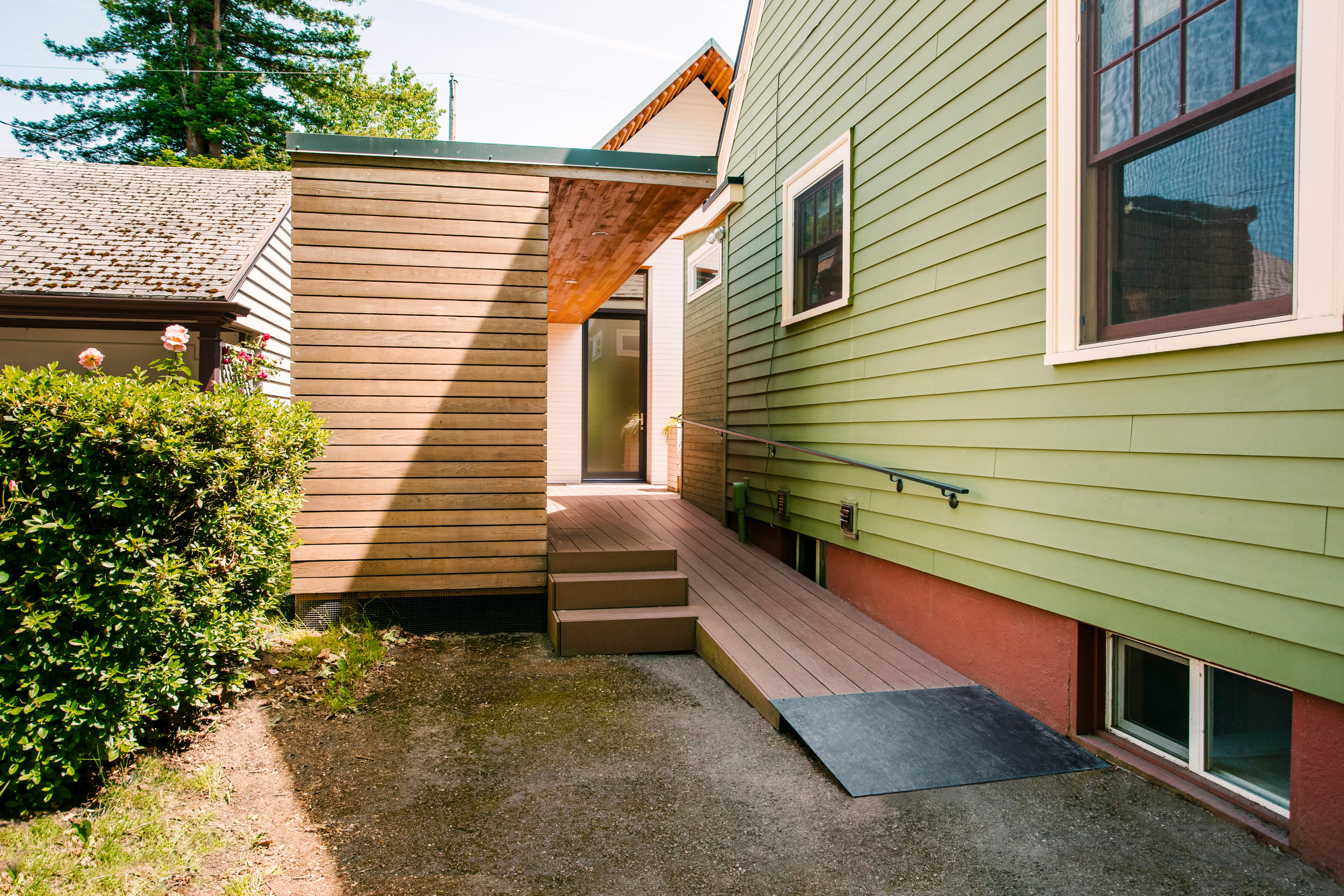 A green house with a wheelchair accessible ramp leading into the entryway.