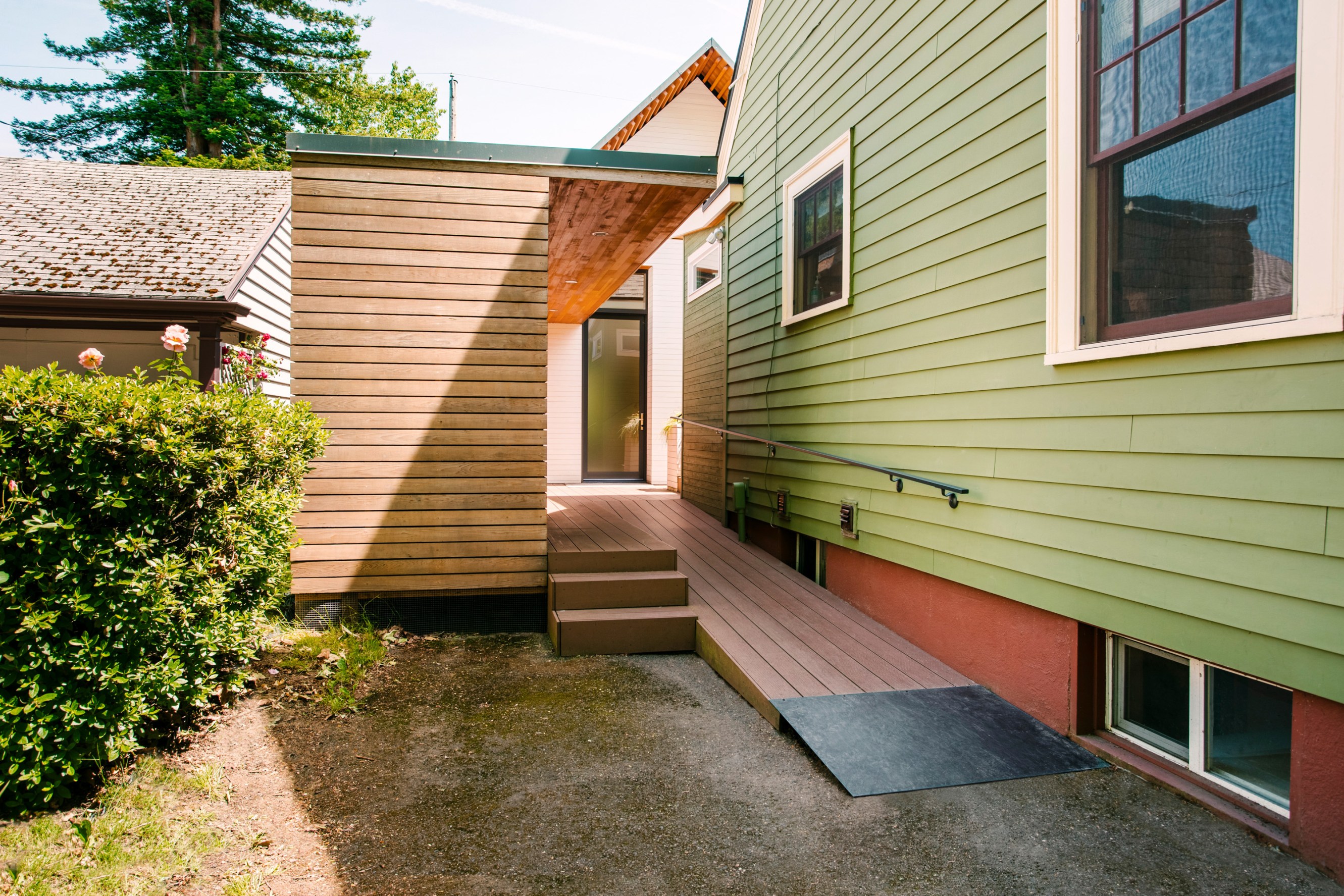A green house with a wheelchair accessible ramp leading into the entryway.