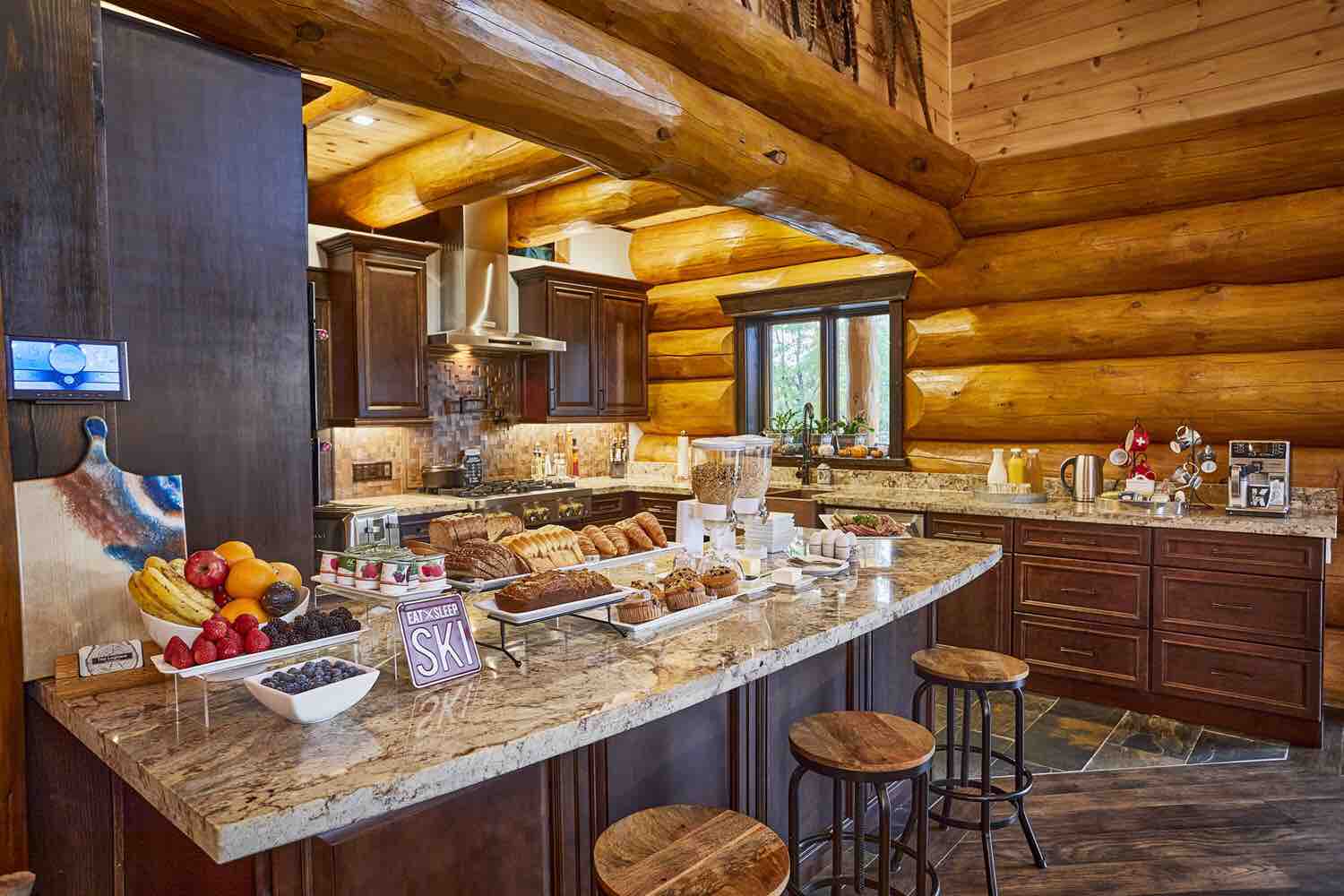 A lavish breakfast spread on a granite countertop in a rustic but modern Swiss-inspired log-walled kitchen.