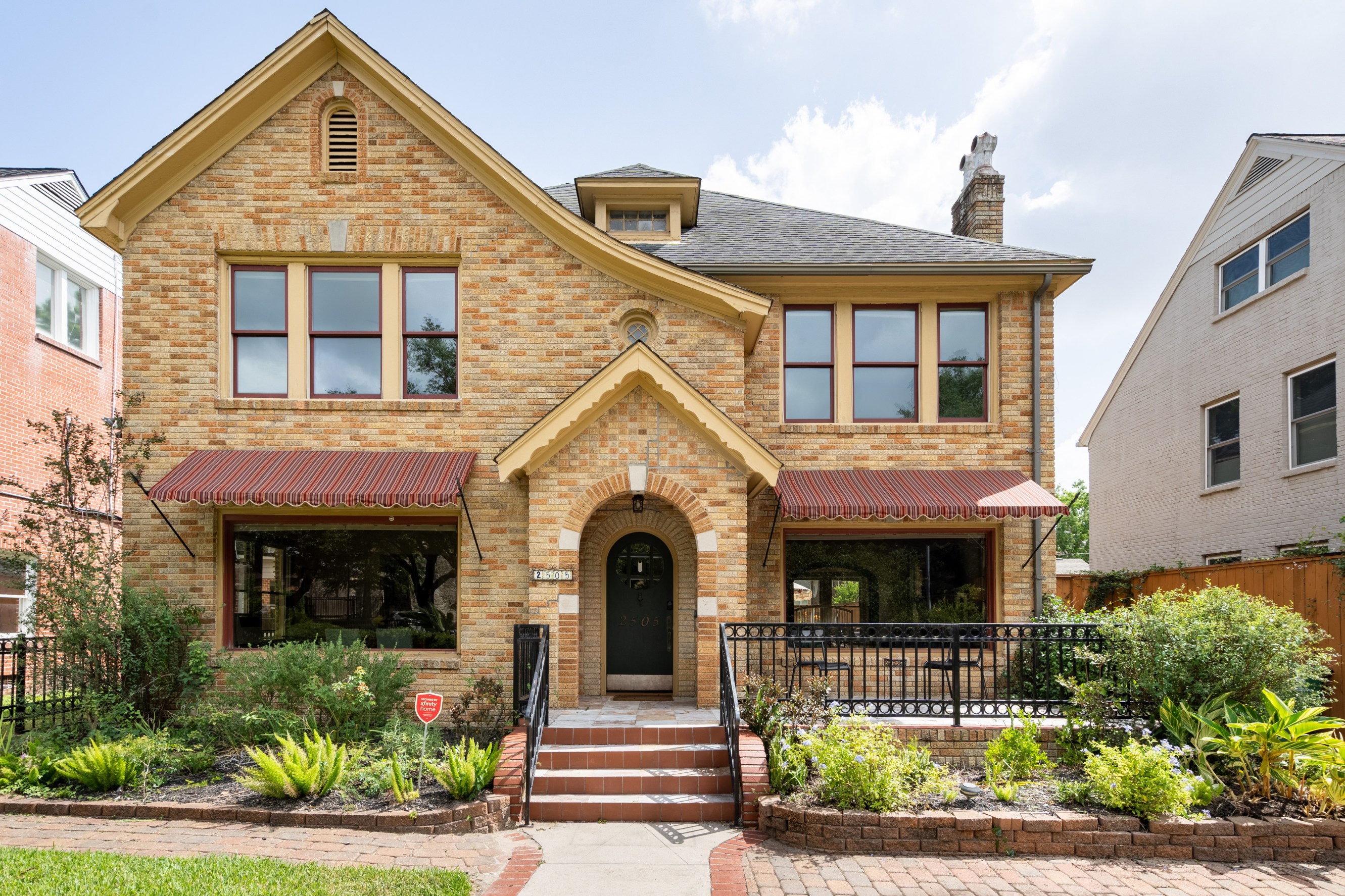 Exterior shot of the home with limestone colored brick and two brown striped awnings on the first floor.