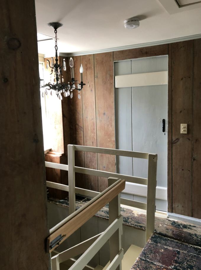 Old upstairs hallway with mini chandelier above the staircase. A blue farm door is at the top of the stairs.