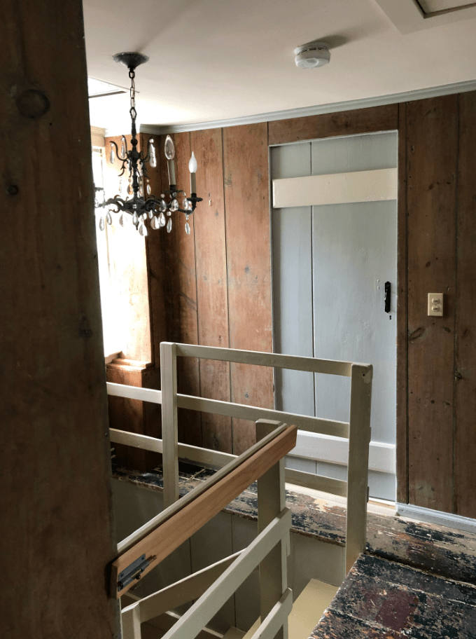 Old upstairs hallway with mini chandelier above the staircase. A blue farm door is at the top of the stairs.