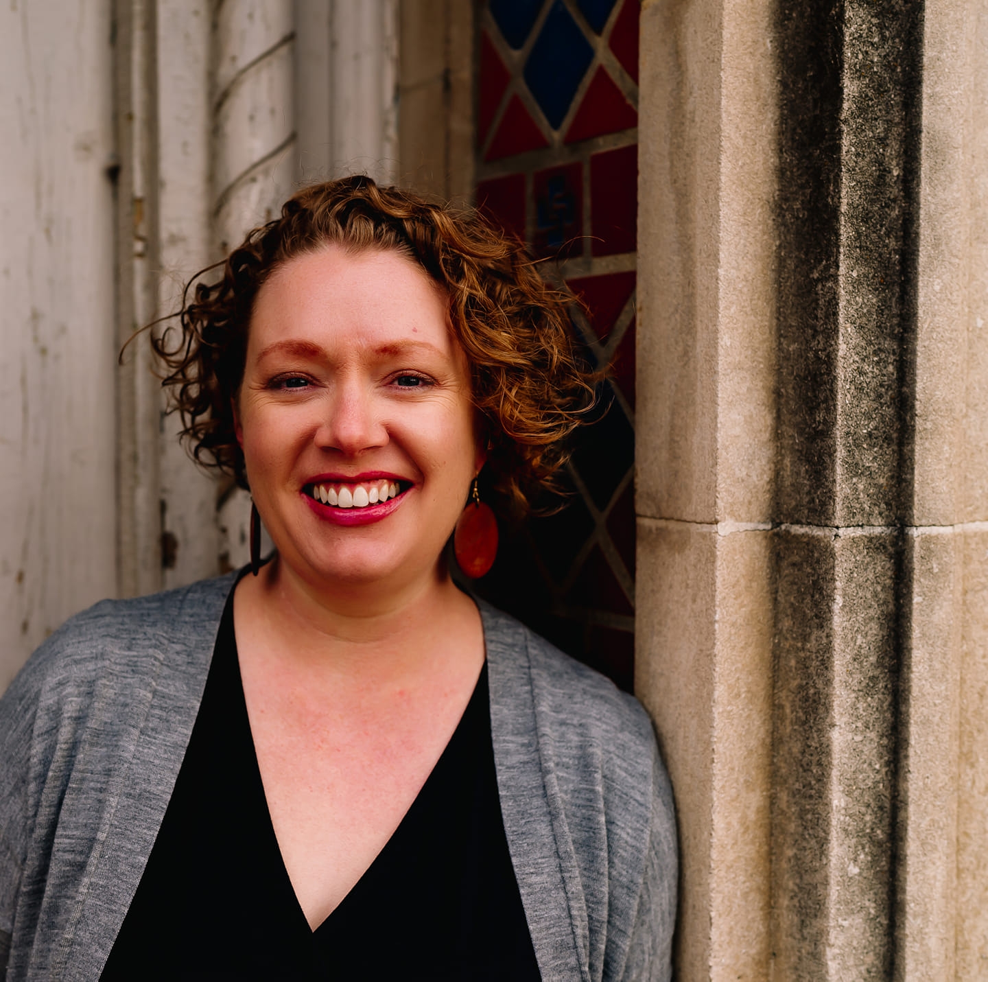 Woman posing and smiling for a photo outside near a building.