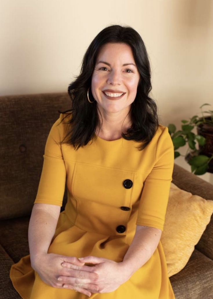 Woman in a yellow dress sitting and posing for a photo with a smile. 
