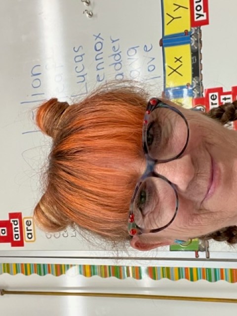 Woman smiling for a photo in front of a whiteboard in a classroom. 