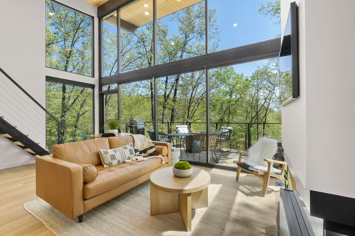 Modern lounge room with floor to ceiling windows looking out onto large trees and bushland.