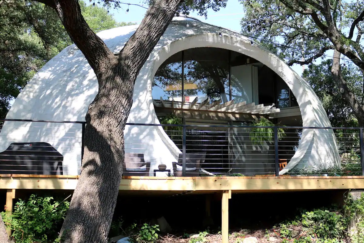 
A white dome house with a circular glass window sitting atop wooden risers. 