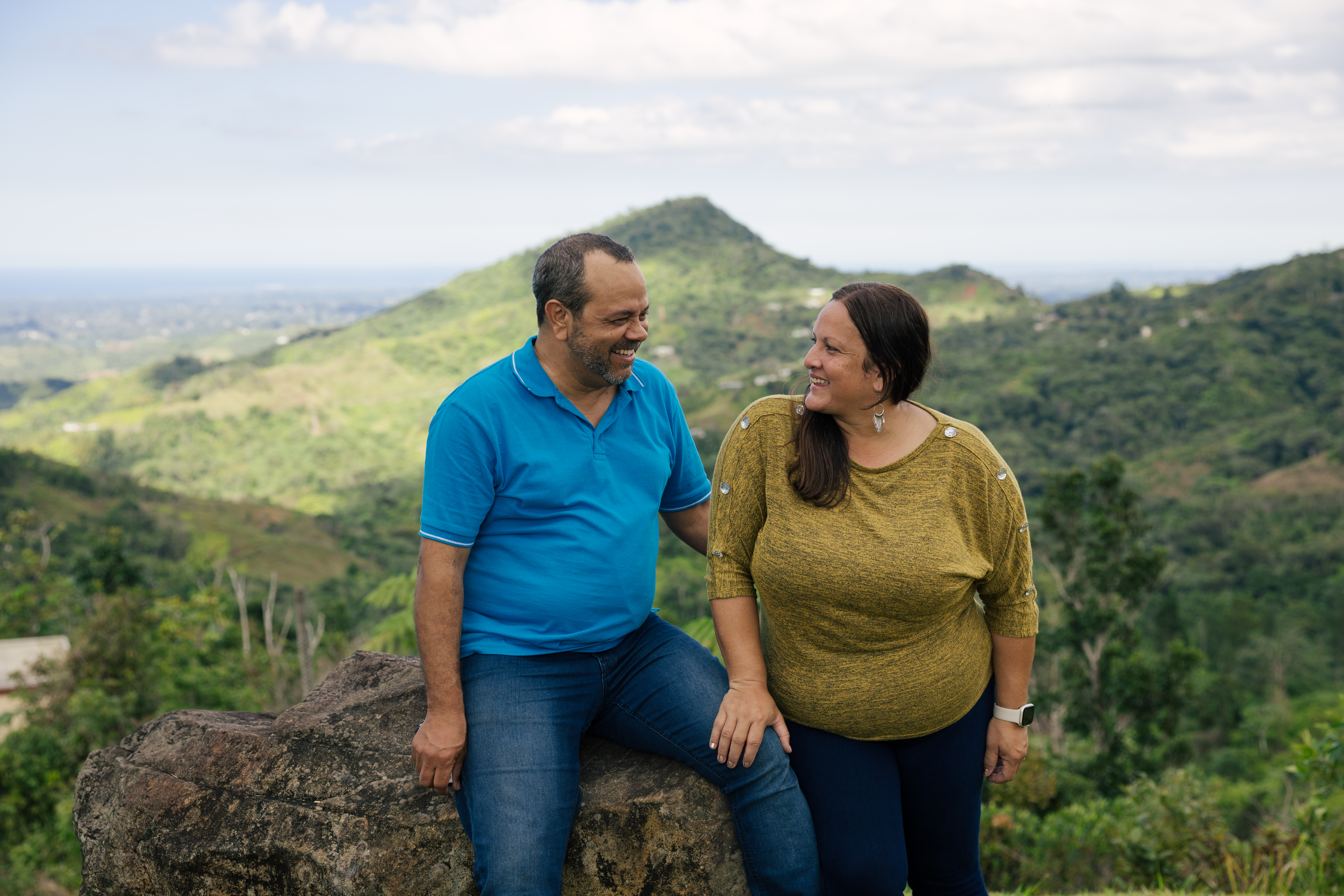 Hombre y mujer, anfitriones de la plataforma, se miran y sonríen. Al fondo un cafetal