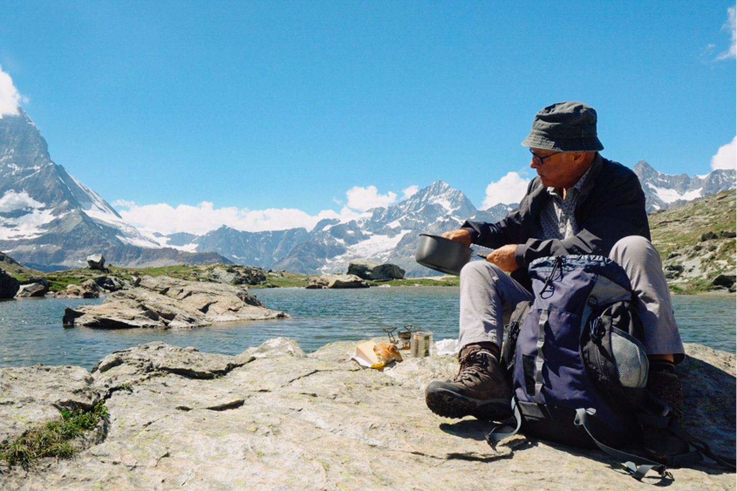 Senderista cocinando en las montañas chilenas, al fondo montañas elevadas con puntas nevadas y abajo lagos