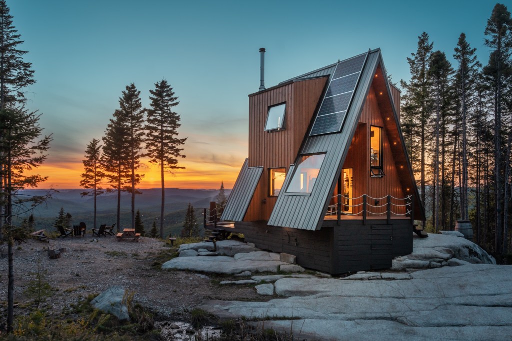 An a-frame cabin in the forest at sunset.