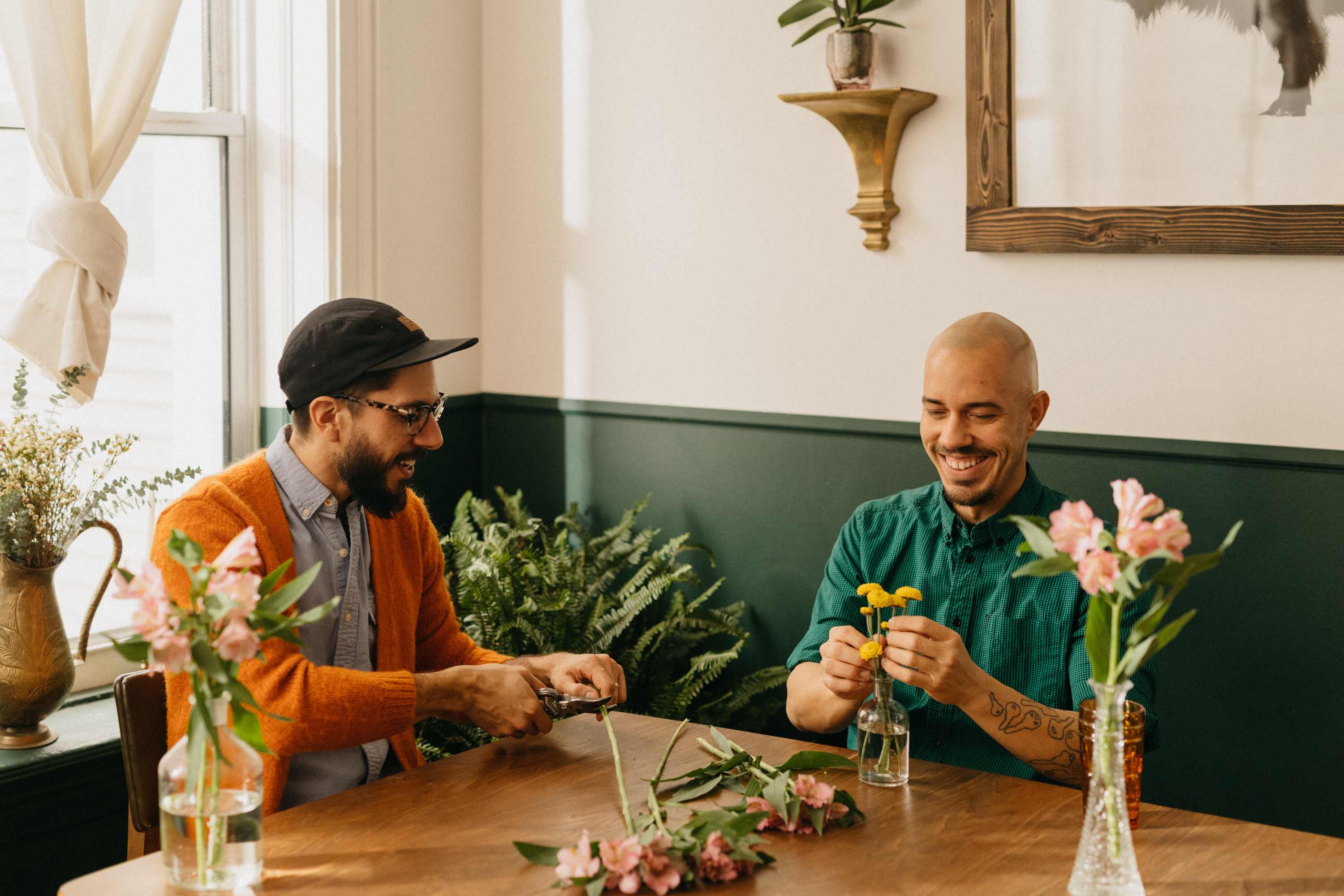 Two men smiling at a table arranging floral bouquets