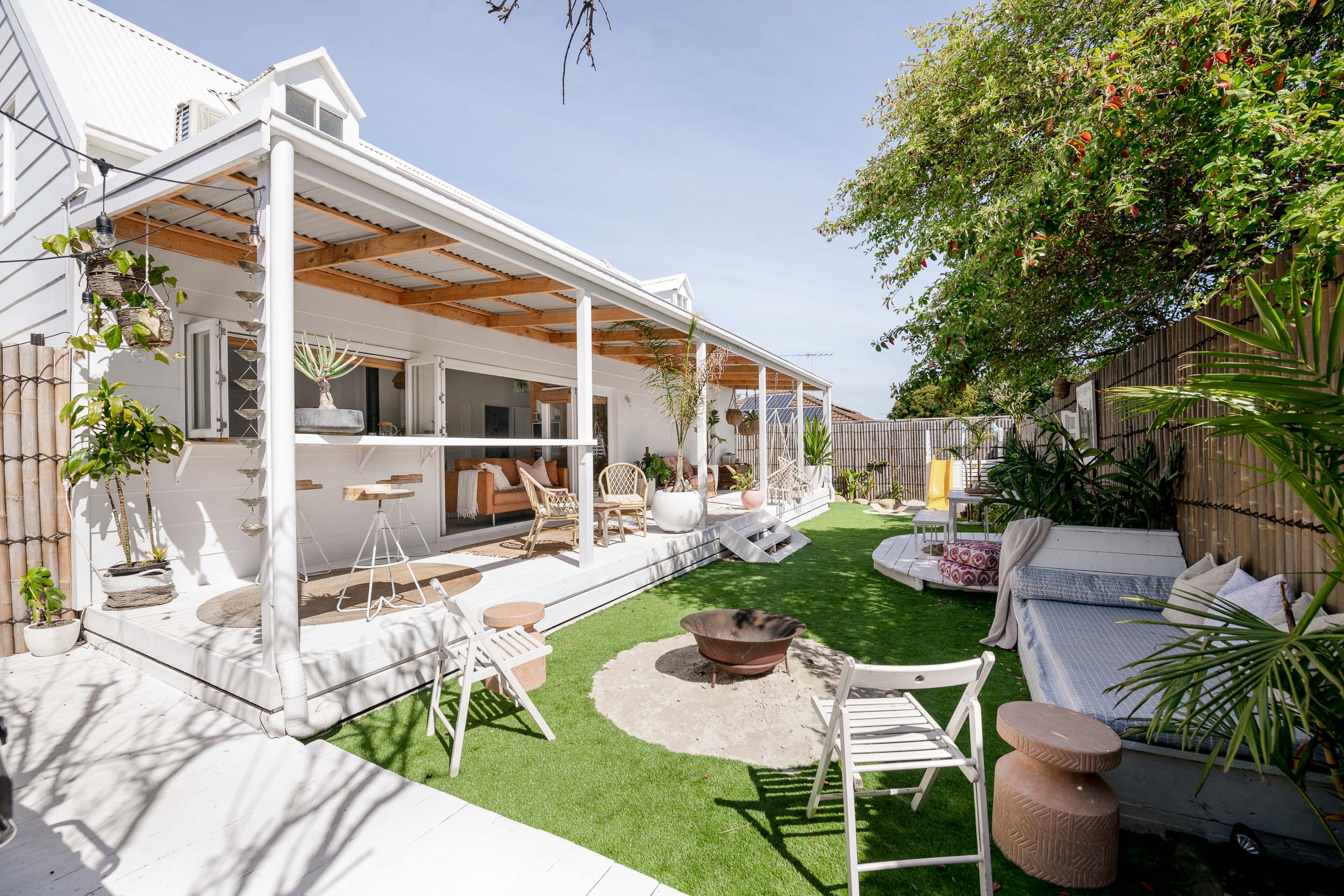 Exterior shot of a brilliant while beach cabin. Lots of garden amenities in the foreground such as a firepit, garden furniture and a slide for kids.