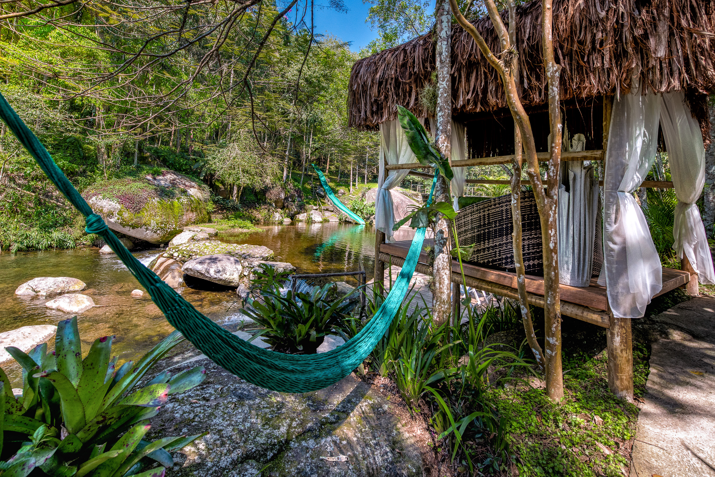 Exterior shot of a chalet in Brazil, erected next to a natural pool and forestry. Waterslide in the background.