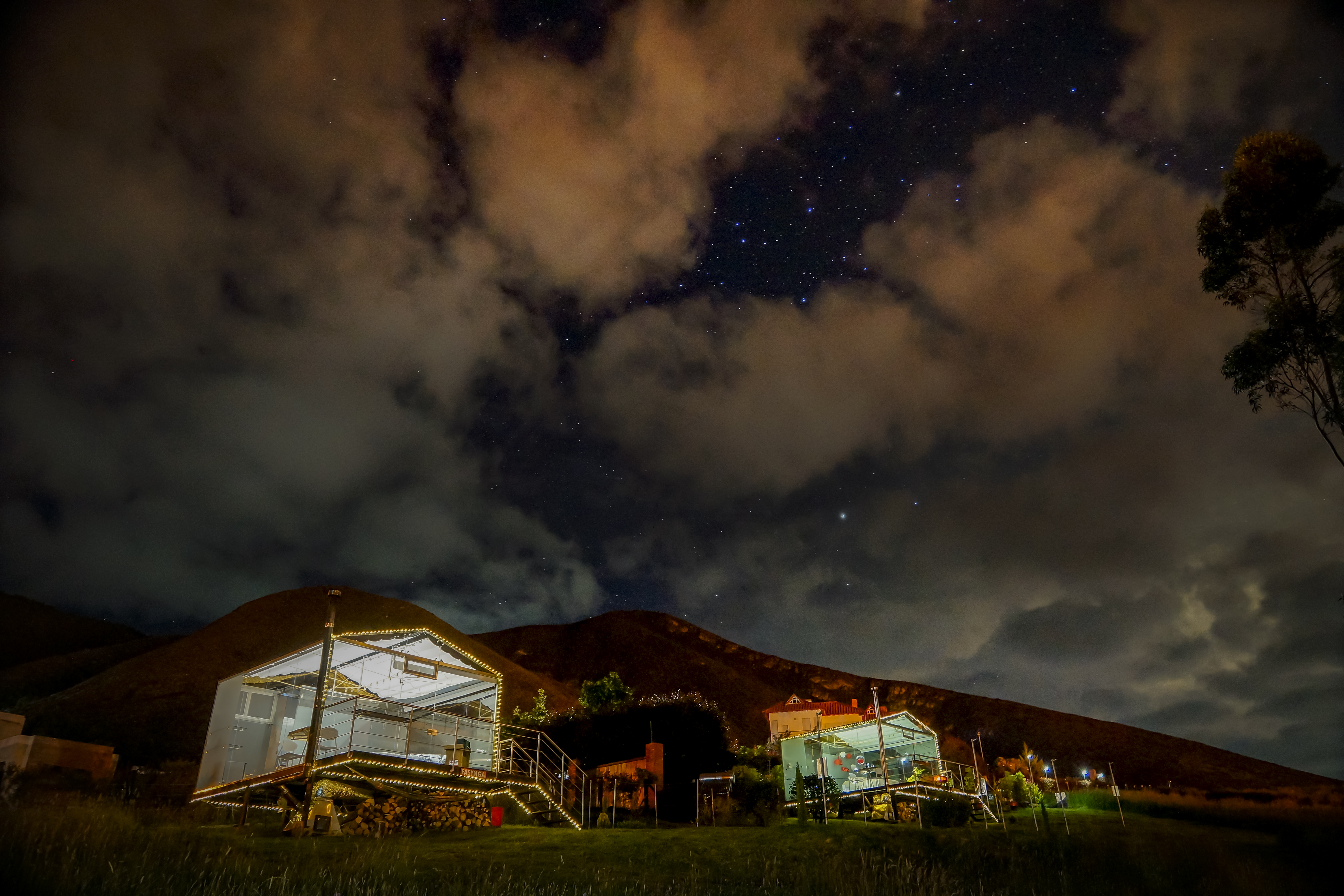 View of two glass cabins in the night with a view of the stars and clouds in the top