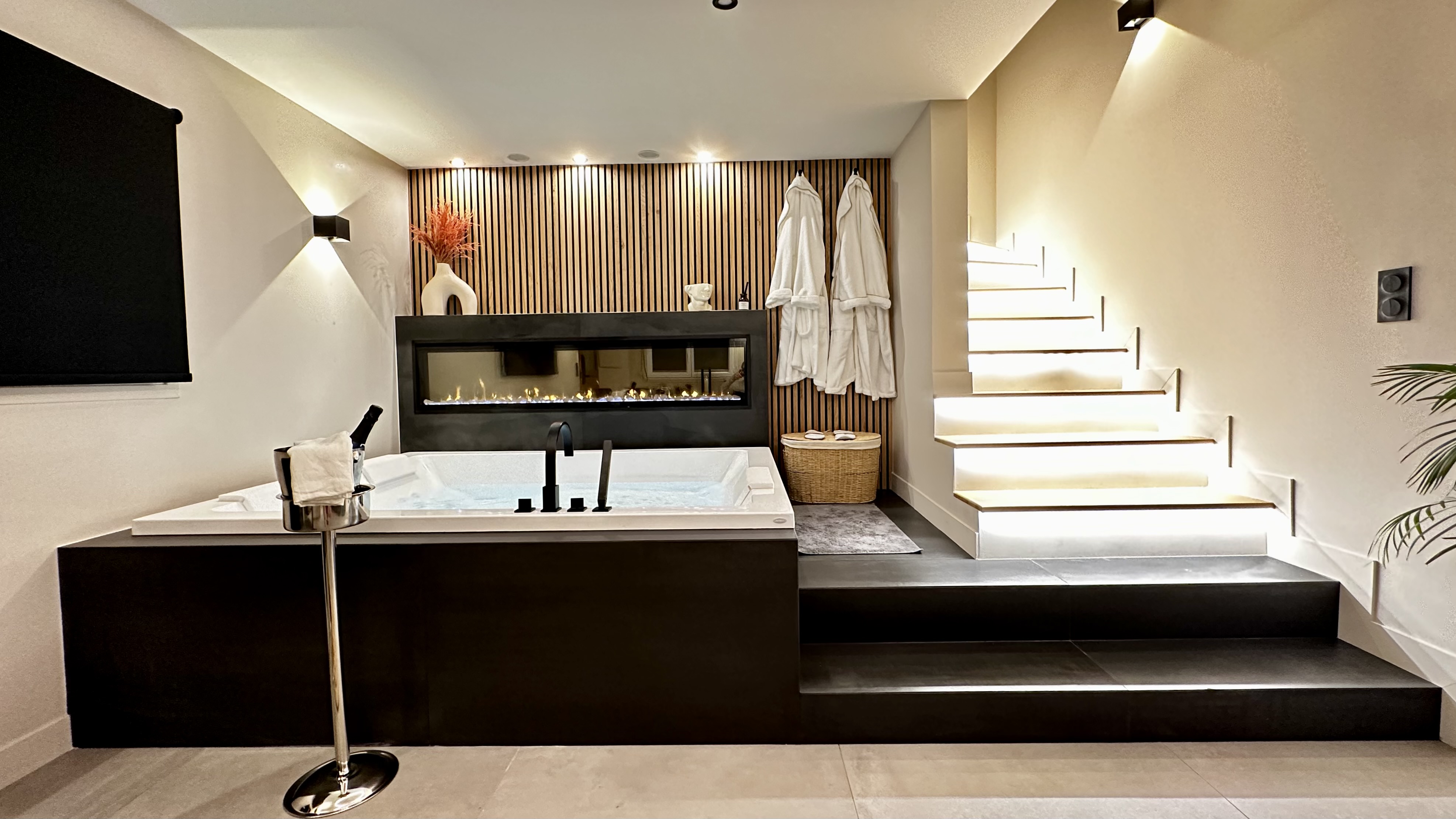 Interior shot of a luxry apartment in L'Île-Saint-Denis, Paris, feauring a hot tub, feature glass-fronted fireplace and an ice bucket with champagne in the foreground.