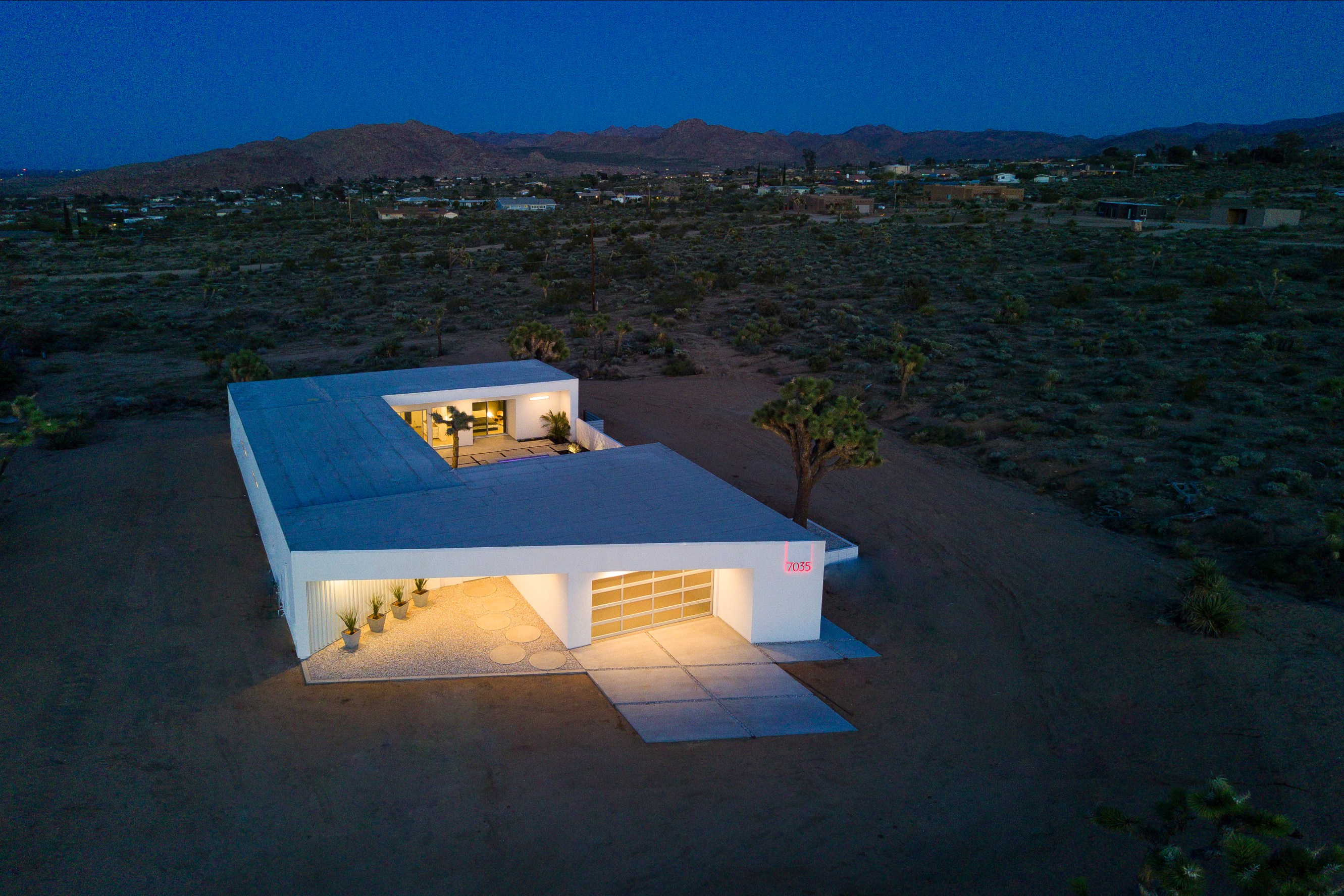 Striking modern desert home from above and at dusk, revealing it's C-shape profile and desert setting