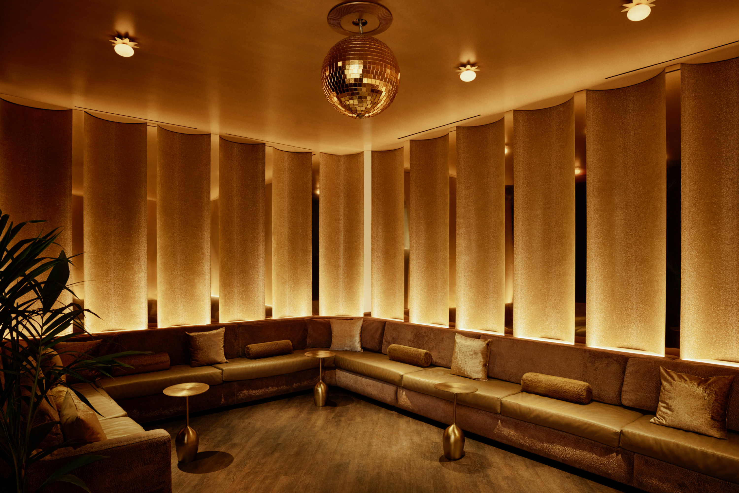 A room with a plush gold couch, small gold tables, and a gold wall with mirrored panels