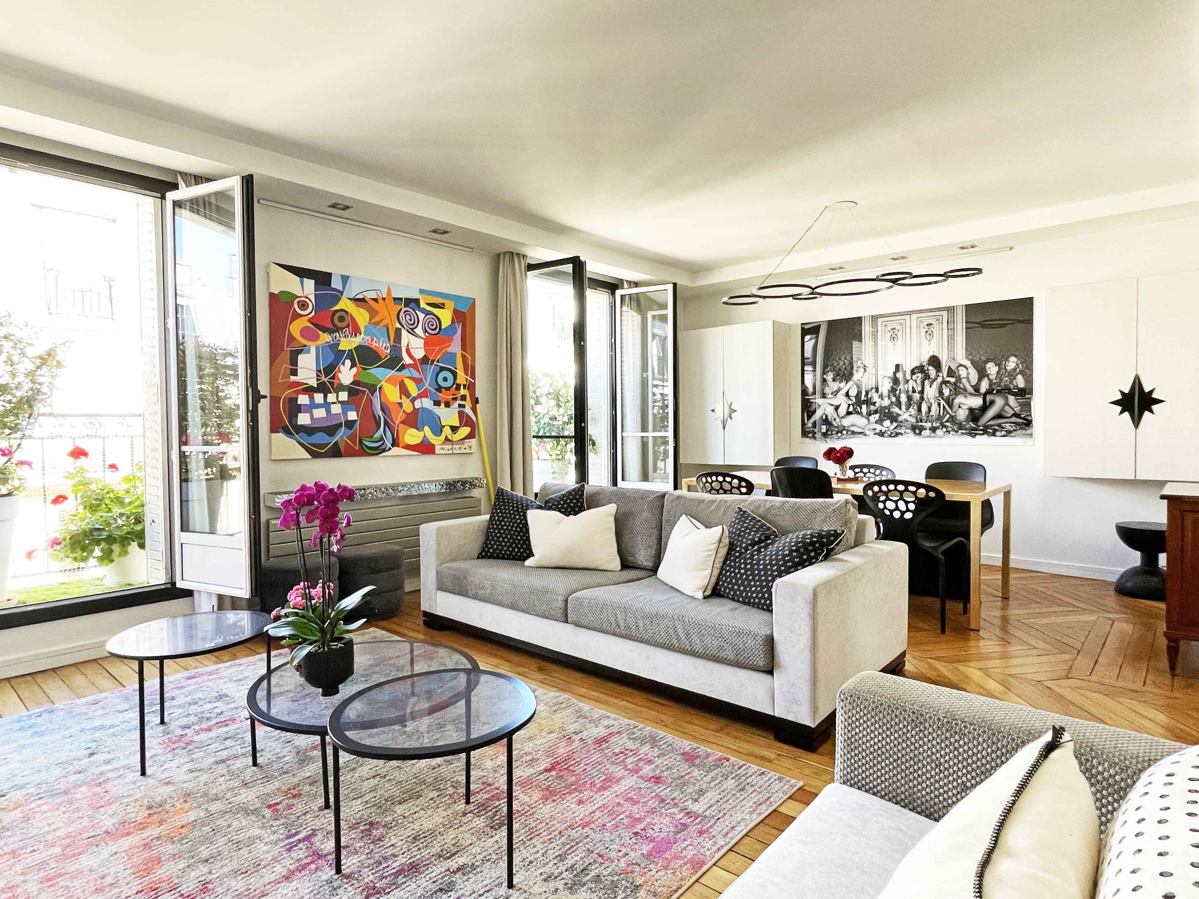 Chic and modern apartment in the Monceau neighborhood of Paris. View is of the living room, featuring a modern grey sofa, a nest of coffee tables and bold artwork on the walls.