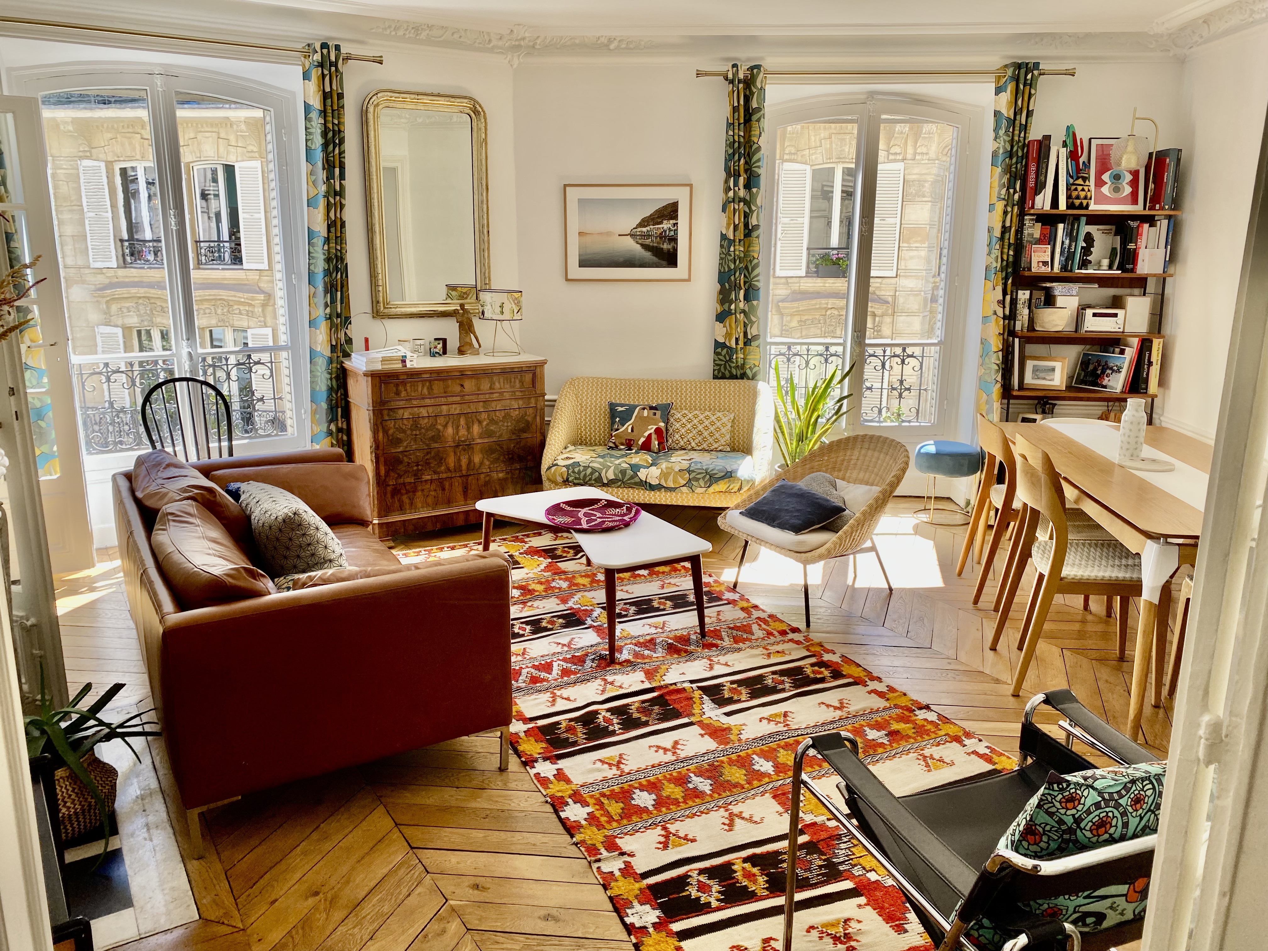 Chic flat in the SoPi district of Paris. View is of a colorful living room, with parquet flooring, a kilim-style rug and an eclectic mix of antique and vintage furniture.