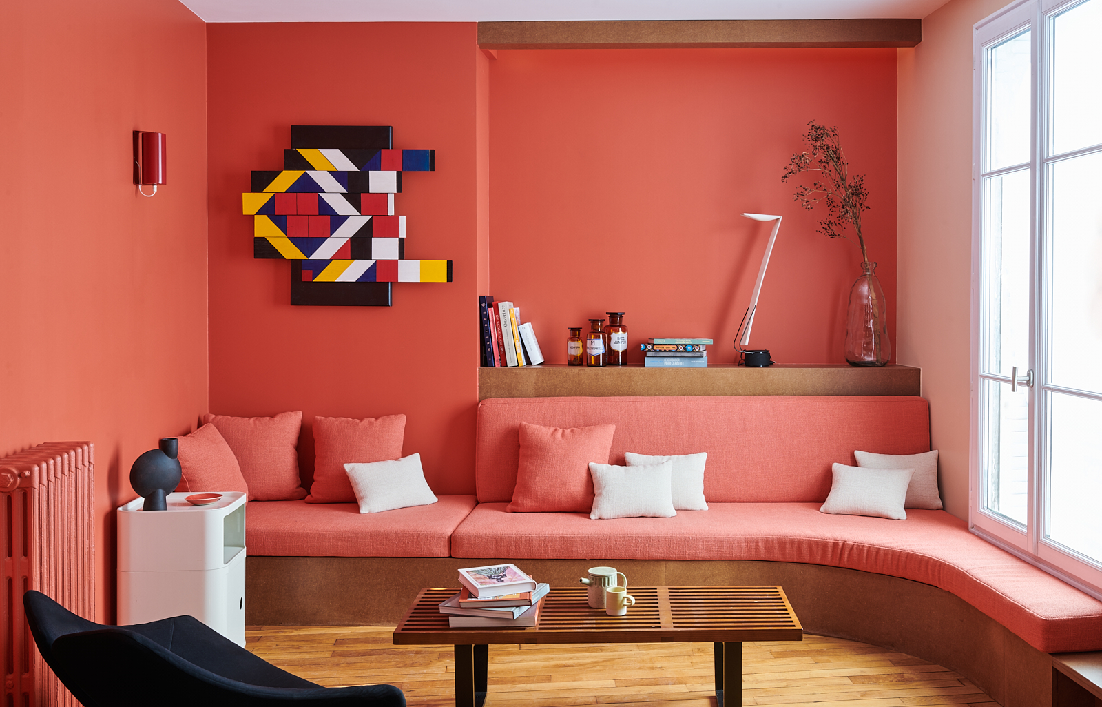 Boldly coloured living room in the T&eacute;l&eacute;graphe neighborhood of Paris. The walls and built-in sofa are the same shade of coral red.