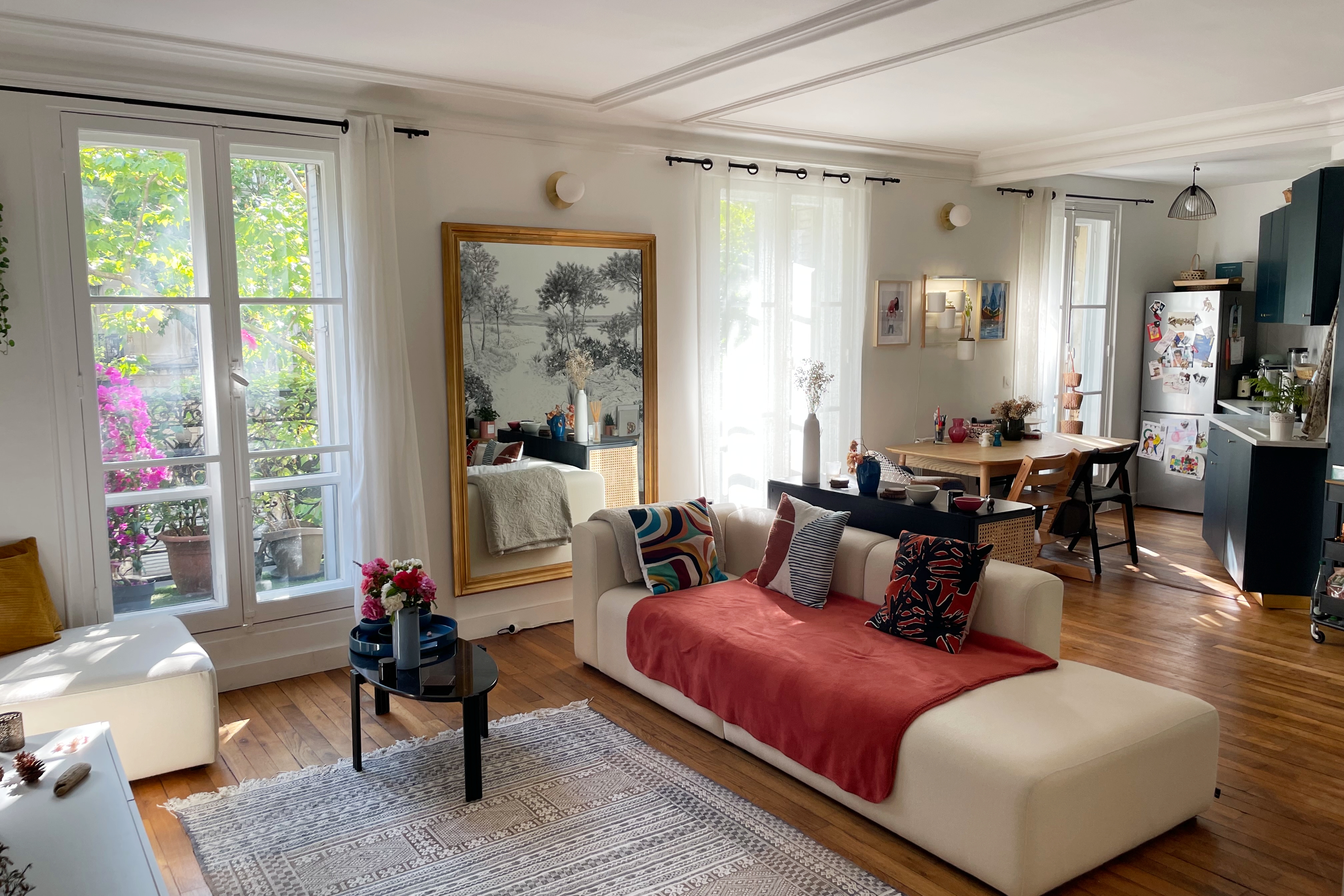 Designer Cocoon in the Porte de Clignancourt neighborhood of Paris. View of a living/ kitchen space, featuring a chaise-style sofa and light streaming in from three traditional french windows.
