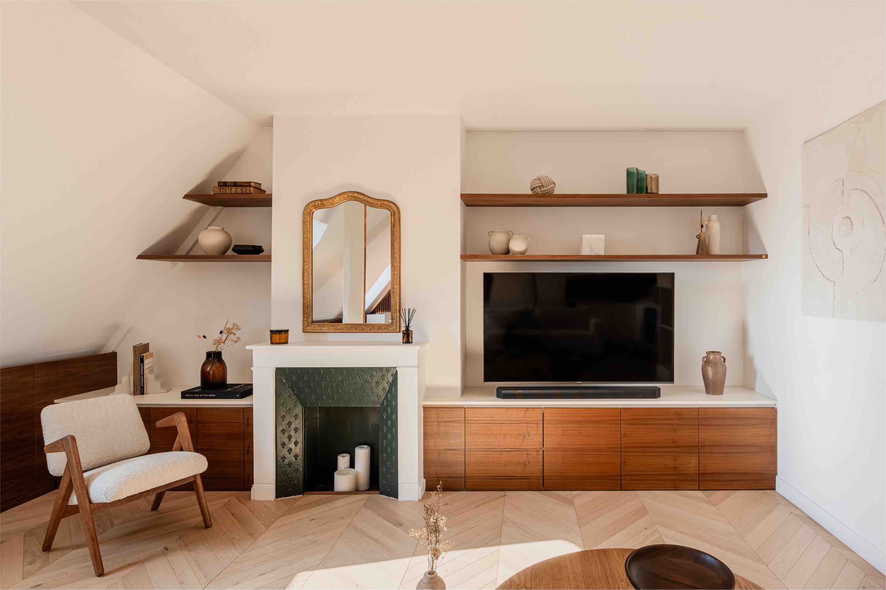 Designer apartment at the Champs-&Eacute;lys&eacute;es in Paris. View is of a stylish living room, built under the eaves, featuring a built-in credenza, a fireplace and a mid century modern armchair.