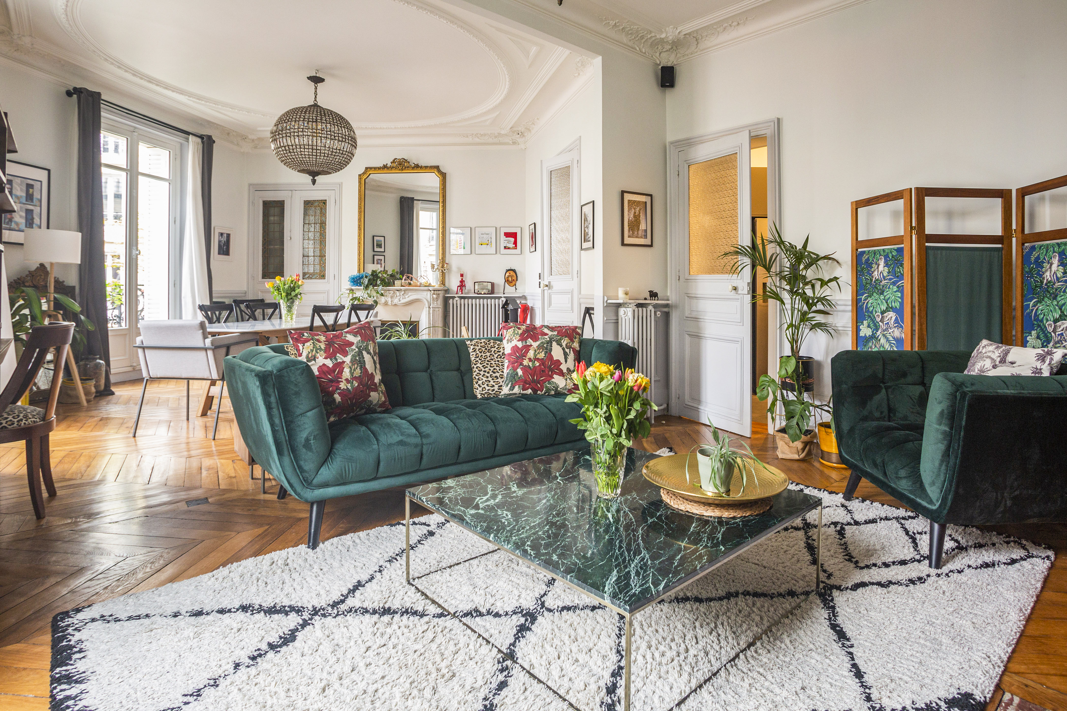 Magnificent Apartment near the Gare du Nord train station in Paris. Shot of the living and dining space, featuring a green velvet sofa, parquet flooring and a vintage chandelier.