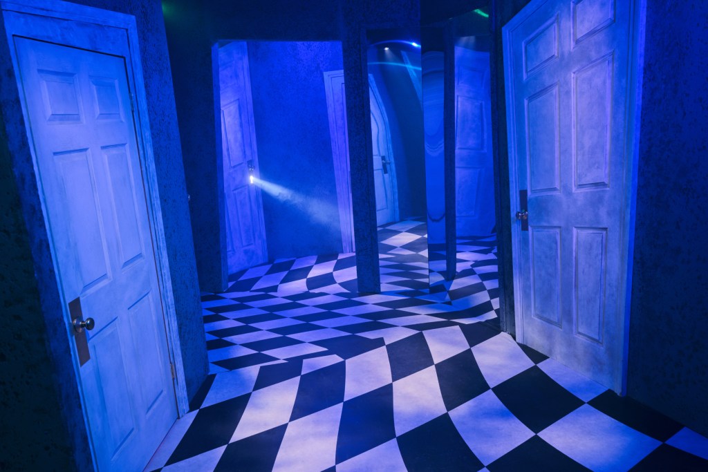 A purple/blue lit hallway with a series of doors and mirrors intentionally disorienting the viewer.