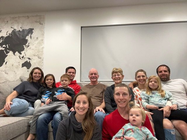 A family of 8 adults and 4 kids sits on a couch smiling