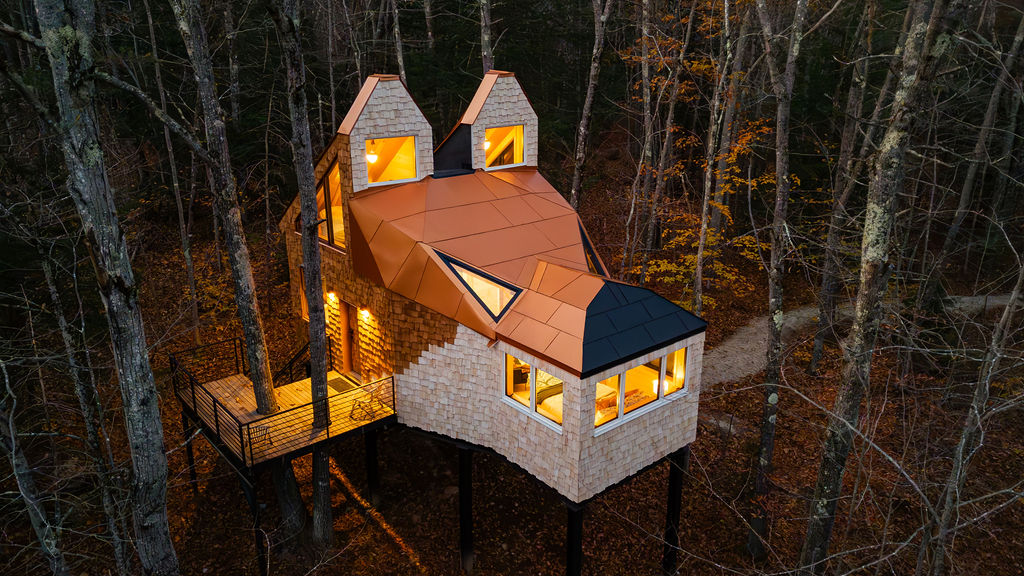 A whimsical treehouse designed to resemble a fox, featuring a unique roof structure that mimics fox ears and a snout. The house is elevated on stilts among a forest of trees, with warm lights glowing from the windows at dusk, creating a cozy and inviting atmosphere.