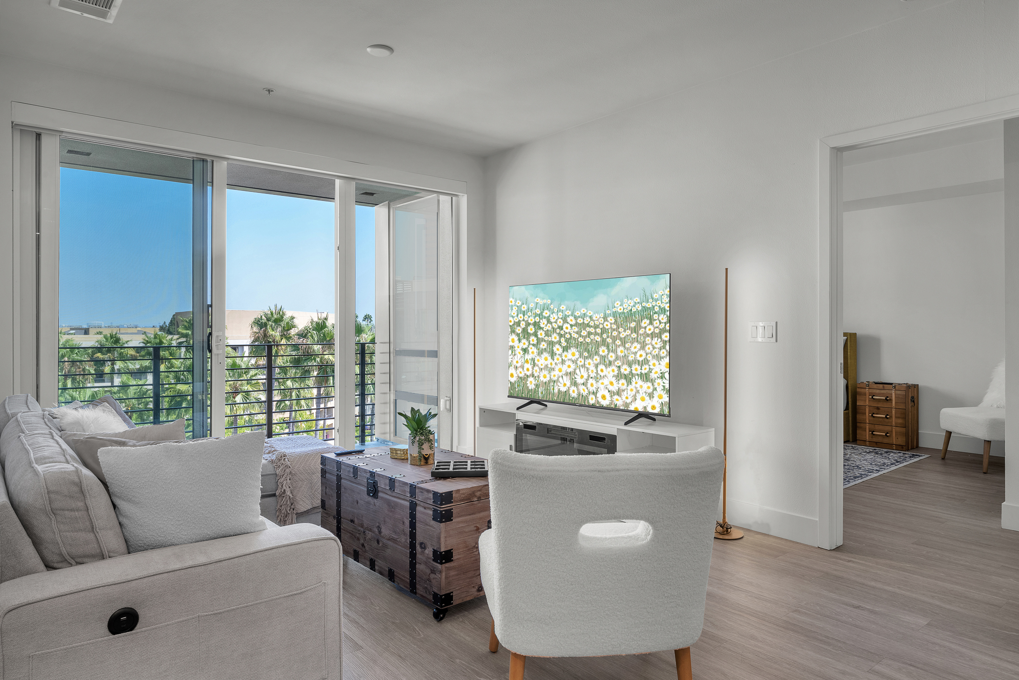 Modern living room featuring a white sofa, wooden chest coffee table, and balcony overlooking palm trees.