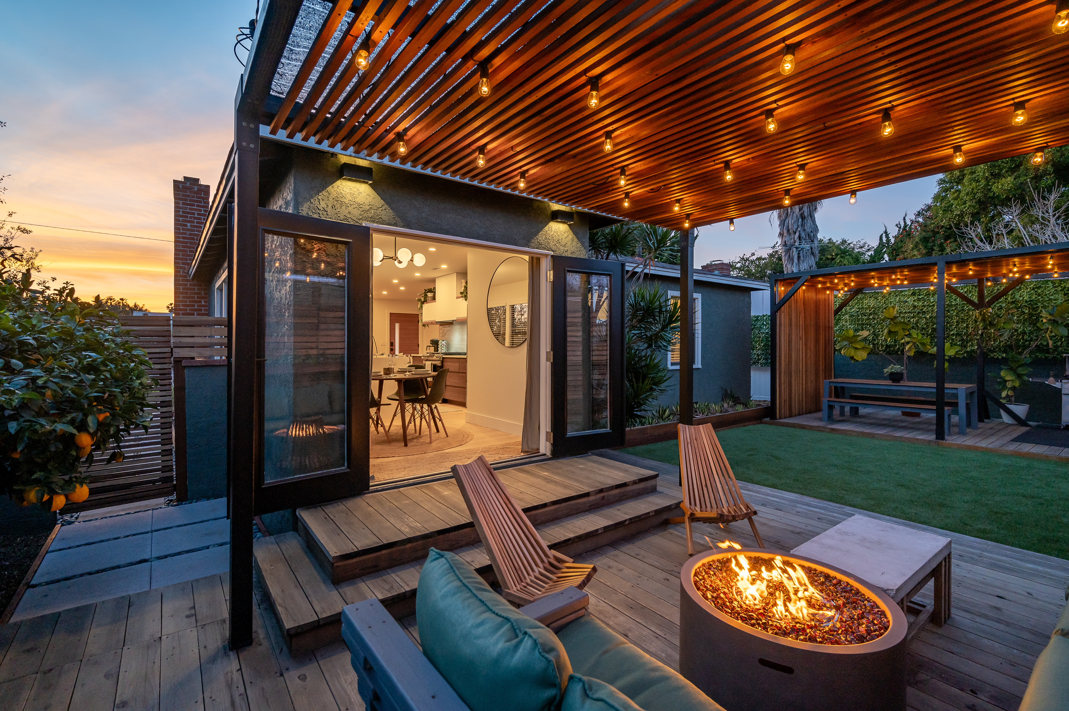 Cozy outdoor patio with wooden pergola, string lights, and a fire pit at dusk.