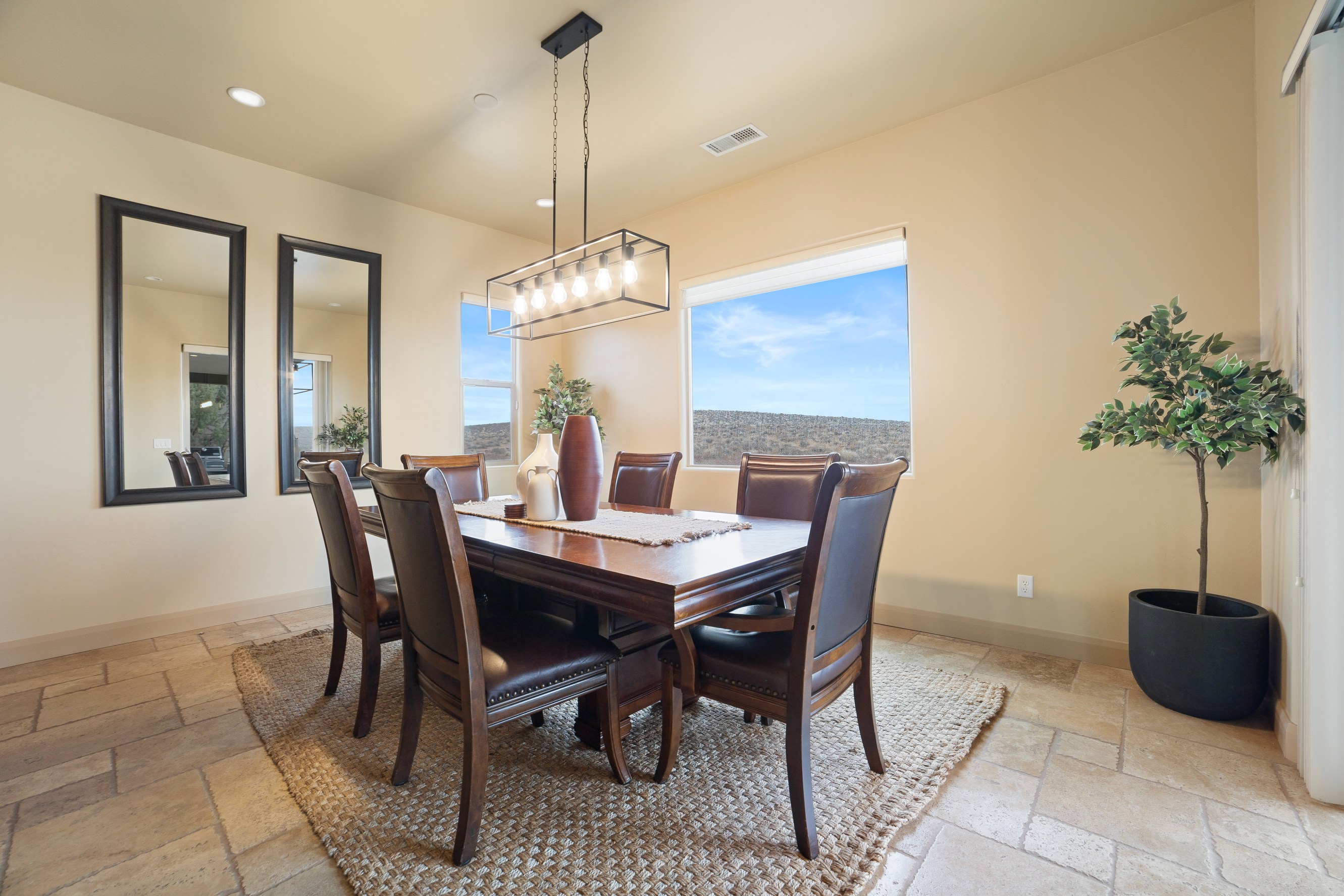 Elegant dining room with a wooden table, six leather chairs, and large windows showing a clear sky.