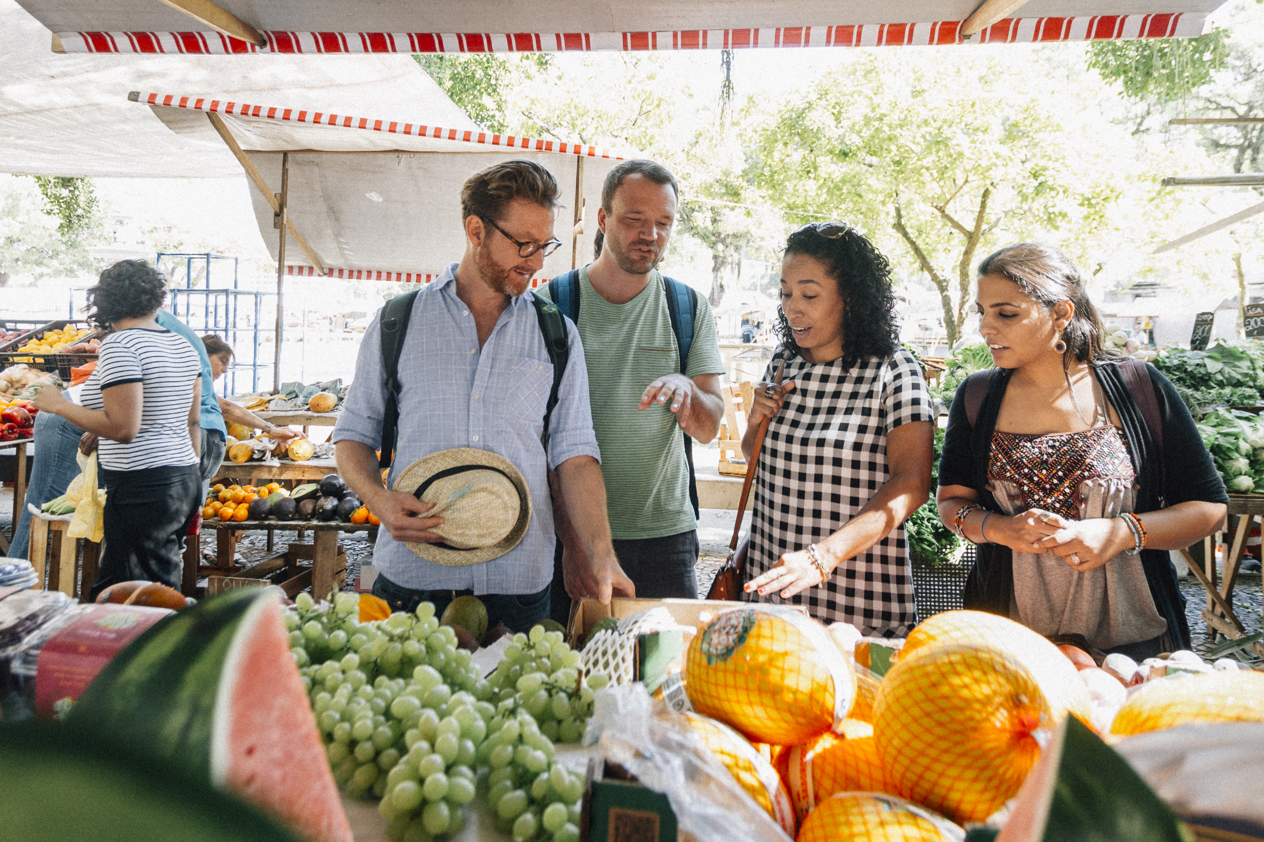 Group of people browsing fresh produce at an outdoor market with a variety of fruits and vegetables on display.